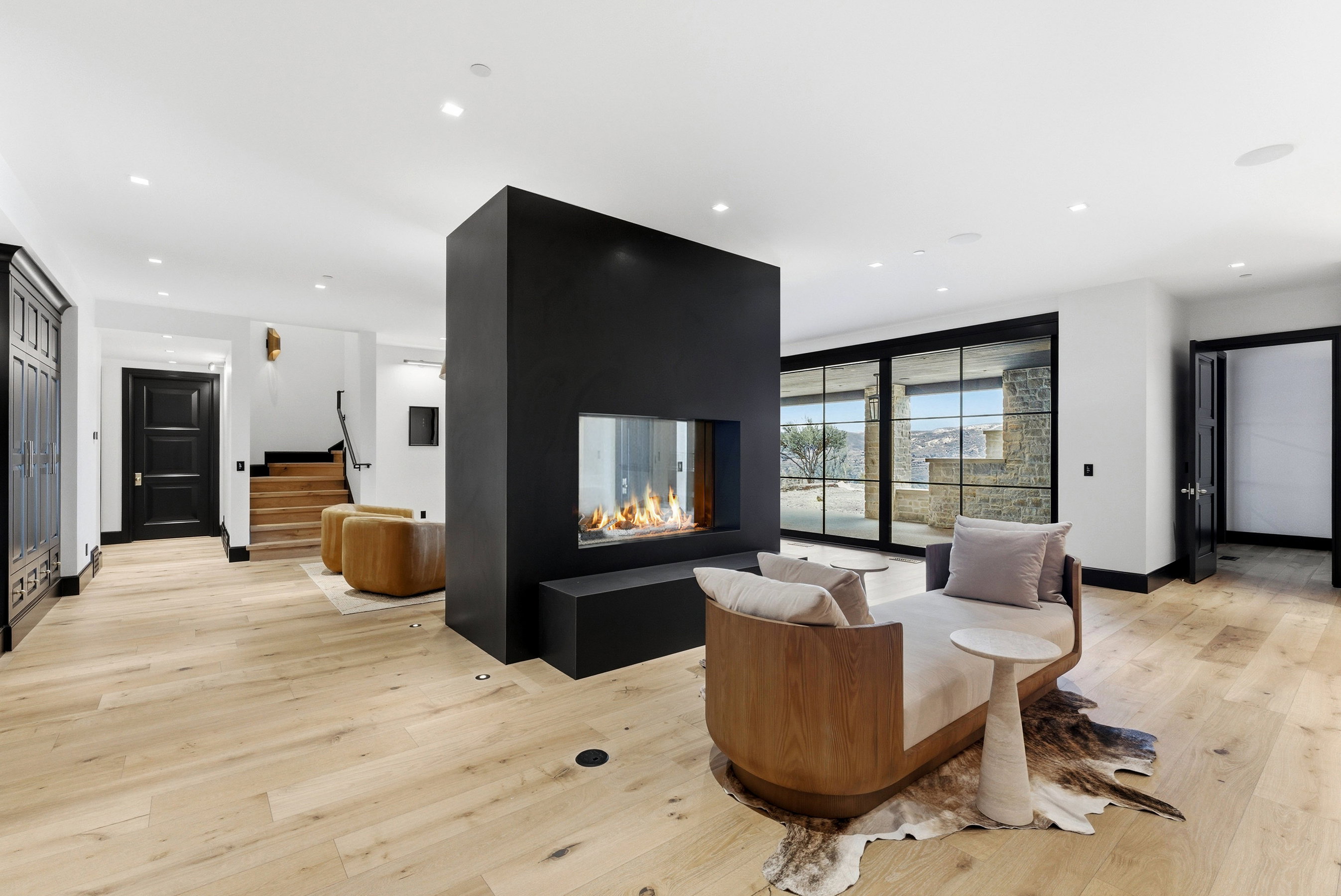 Open-concept living space with light wood-finish flooring, a two-sided contemporary fireplace with a black surround, and expansive sliding glass doors