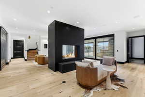 Open-concept living space with light wood-finish flooring, a two-sided contemporary fireplace with a black surround, and expansive sliding glass doors