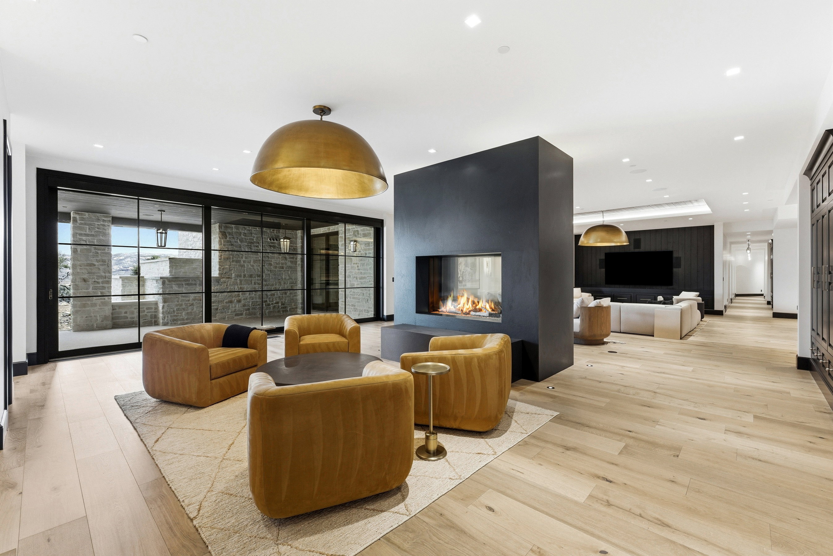 Open-concept living area featuring light wood-finish flooring, a double-sided modern fireplace with a dark surround, and a large brass dome pendant light