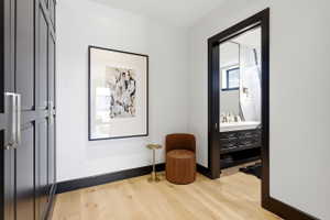 Light wood-finish flooring extending from a hallway into a bathroom with a dark wood vanity, white countertop, and dual sinks