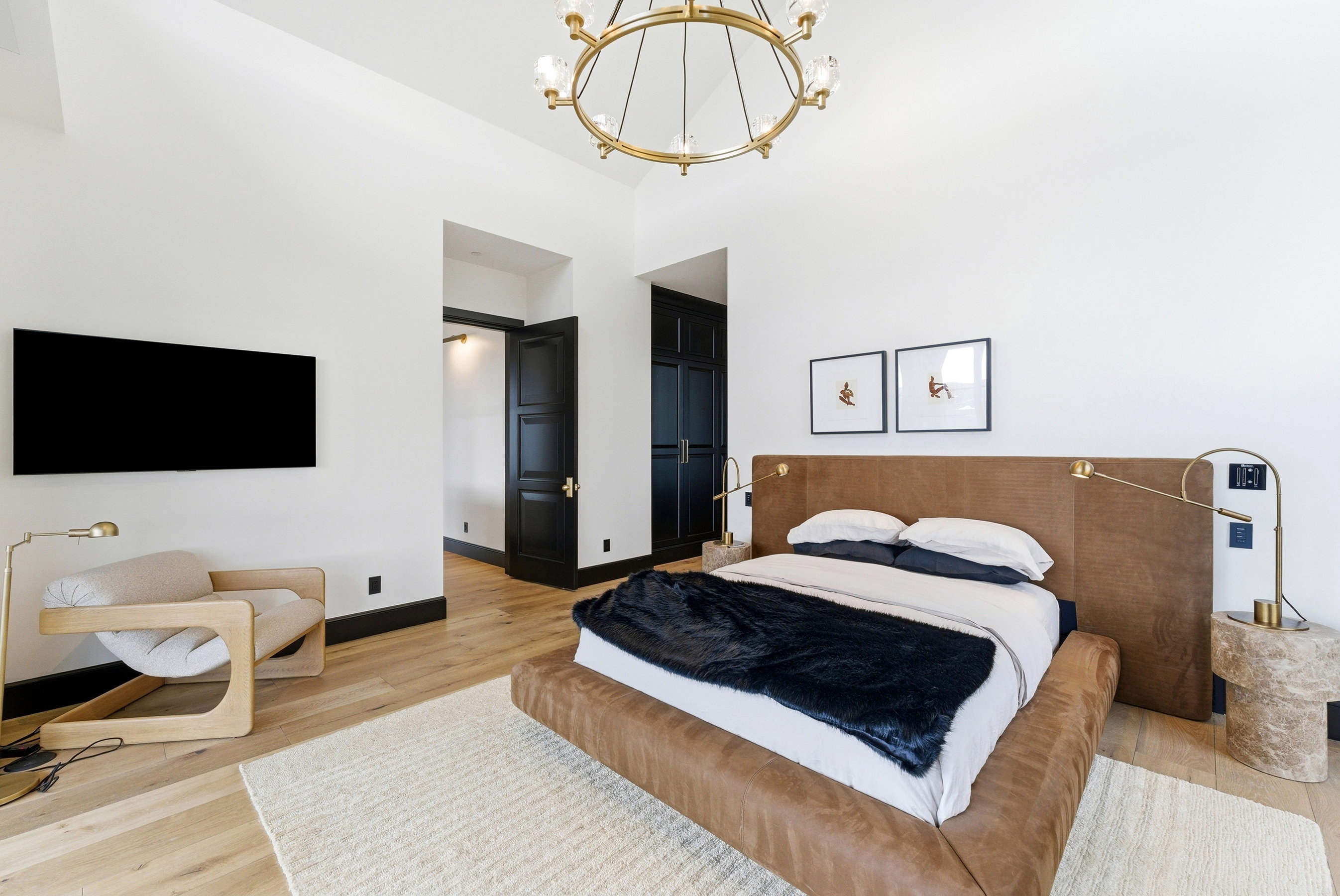 Vaulted ceiling with an ornate chandelier, light wood-finish flooring, dark paneled doors, and built-in closet storage