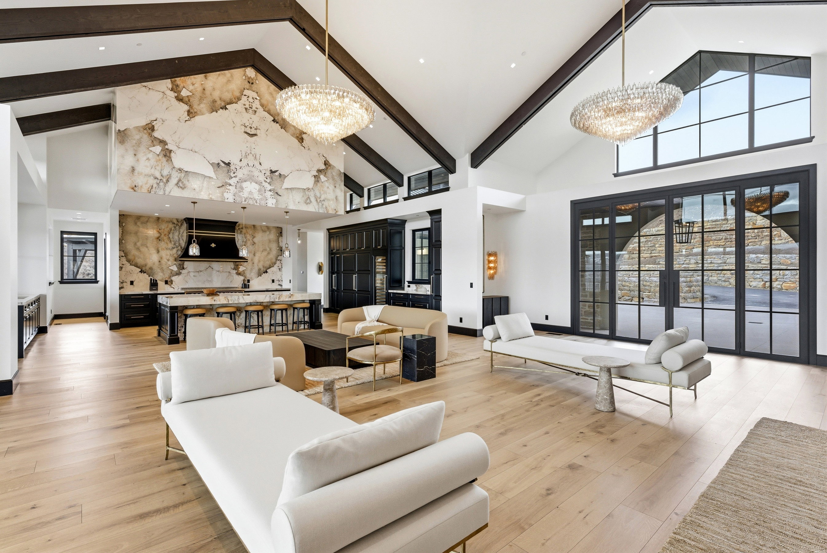 Spacious great room featuring vaulted ceilings with exposed wood beams, light wood-finish flooring, and a large kitchen with a stone-accented wall and a substantial island