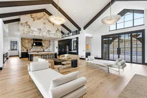 Spacious great room featuring vaulted ceilings with exposed wood beams, light wood-finish flooring, and a large kitchen with a stone-accented wall and a substantial island