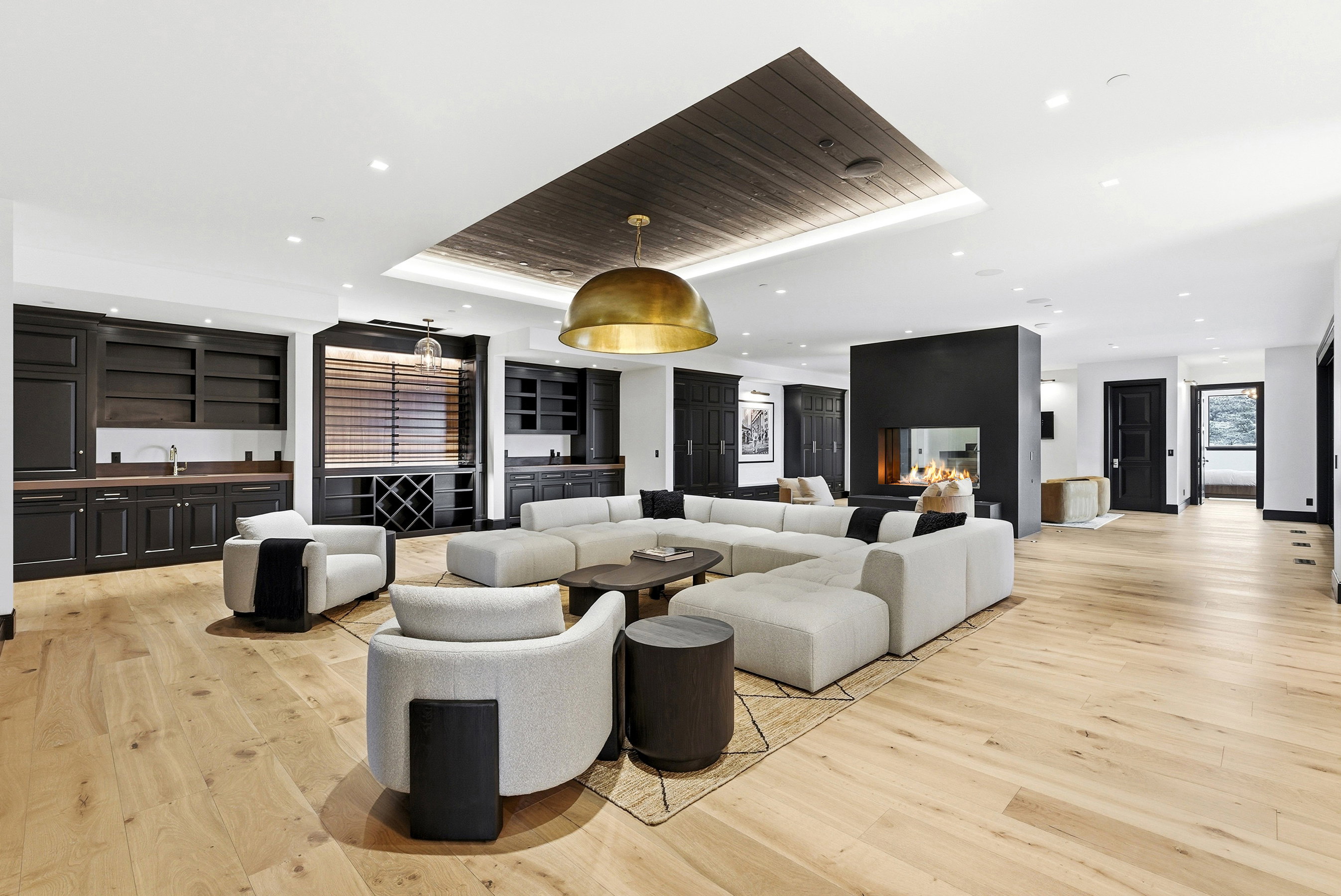 Spacious entertaining area featuring light wood-finish flooring, a recessed fireplace, built-in cabinetry with a wet bar, a dark wood paneled ceiling accent, and recessed lighting
