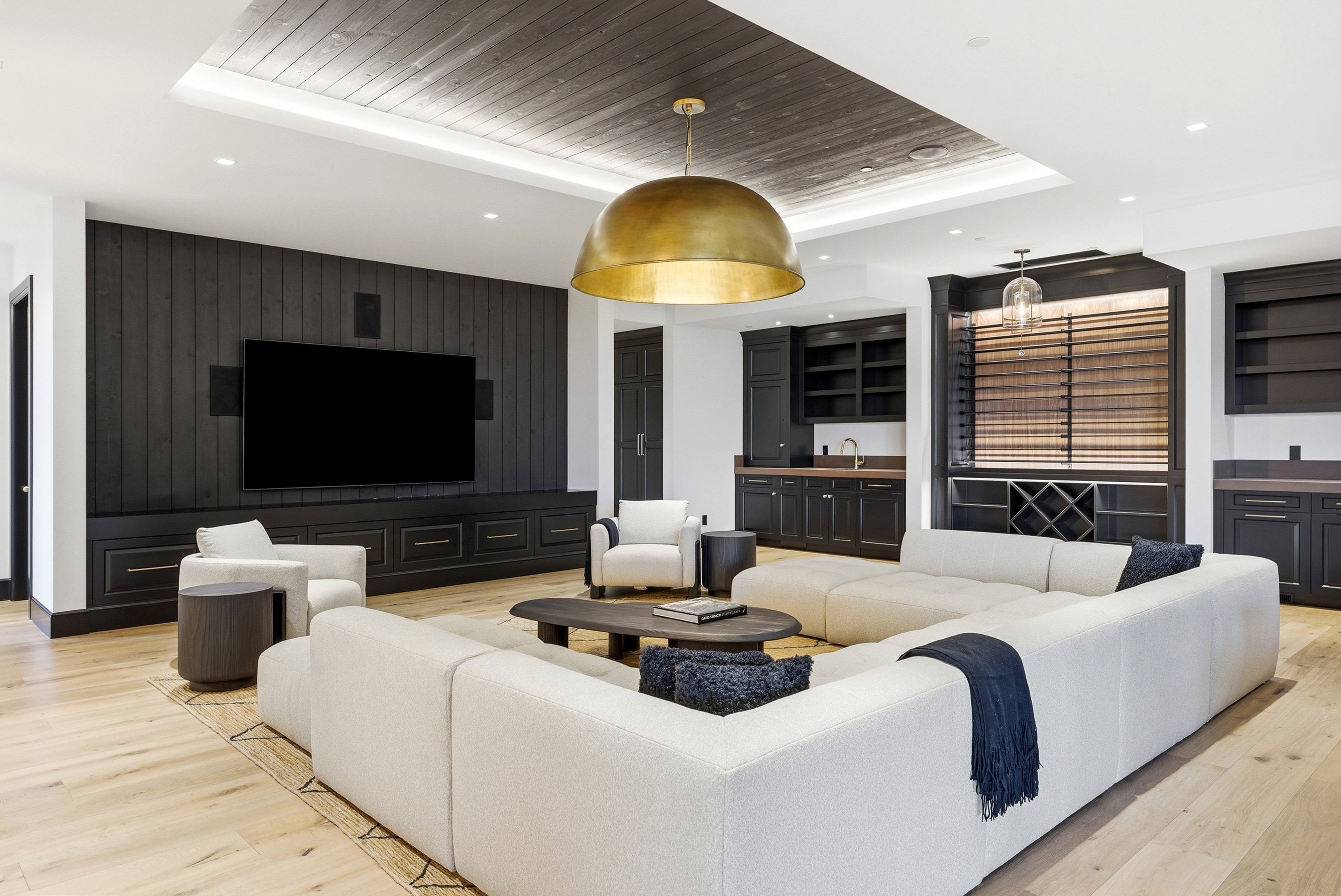 Spacious common area featuring a dark wood plank accent wall with integrated media console, two built-in wet bars with dark wood cabinetry and countertops, and wood-finish flooring