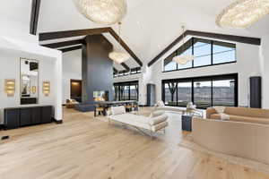 Expansive living space featuring light wood-finish flooring, a vaulted ceiling with dark wood beams, and a floor-to-ceiling fireplace with an integrated hearth