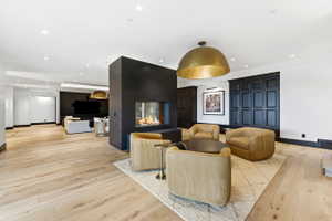 Open-concept room featuring a modern linear fireplace with a dark surround, blonde wood-finish flooring, recessed lighting, and dark paneling