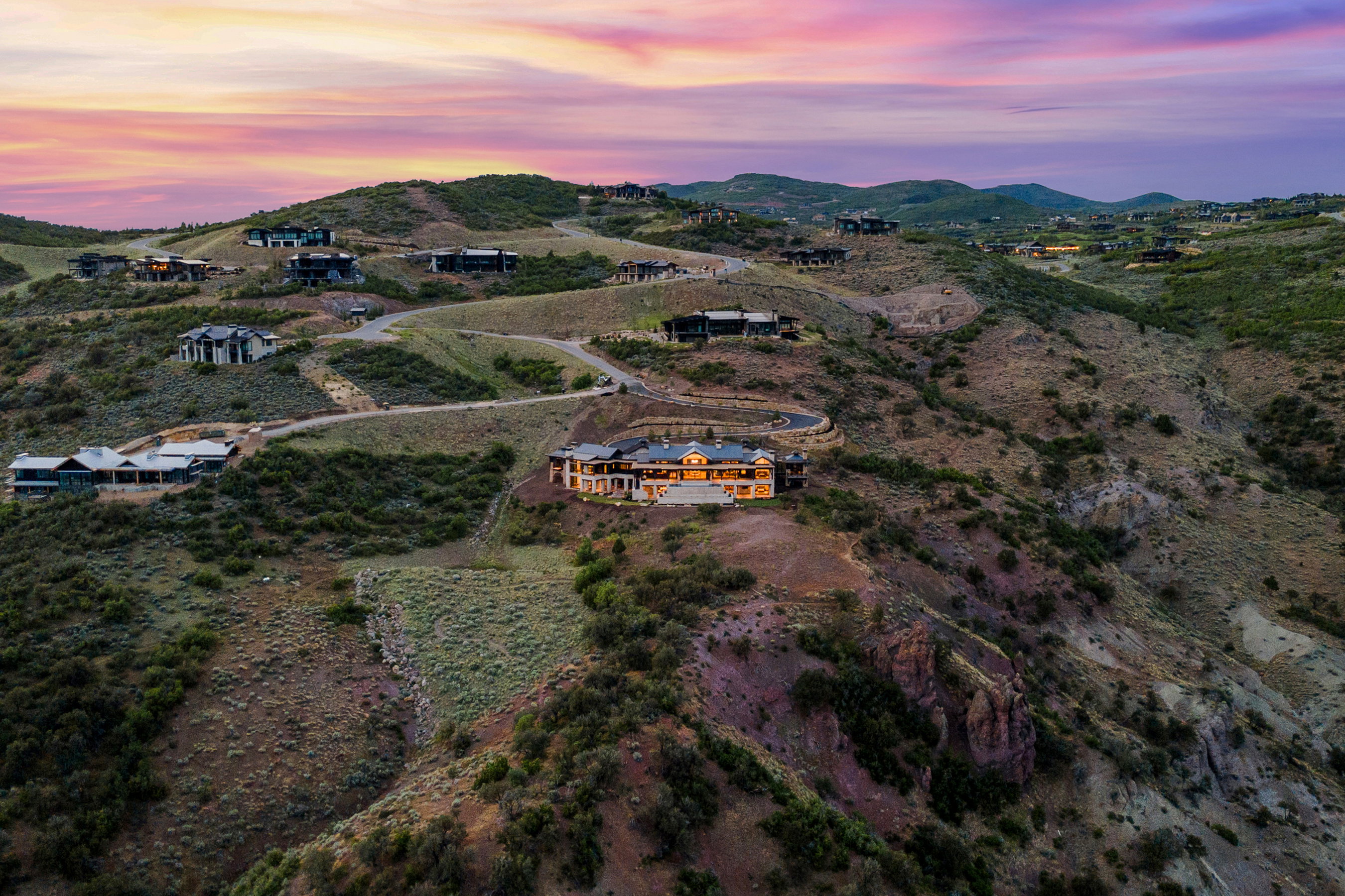 Expansive hillside property featuring a multi-level residence with exterior lighting, a paved driveway, and established landscaping