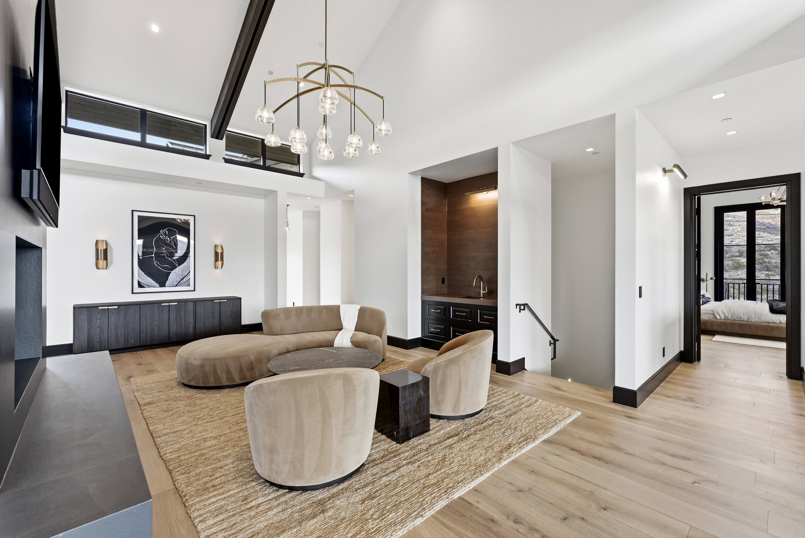 Spacious room featuring vaulted ceilings with exposed beams, wood-finish flooring, and a built-in wet bar with dark cabinetry