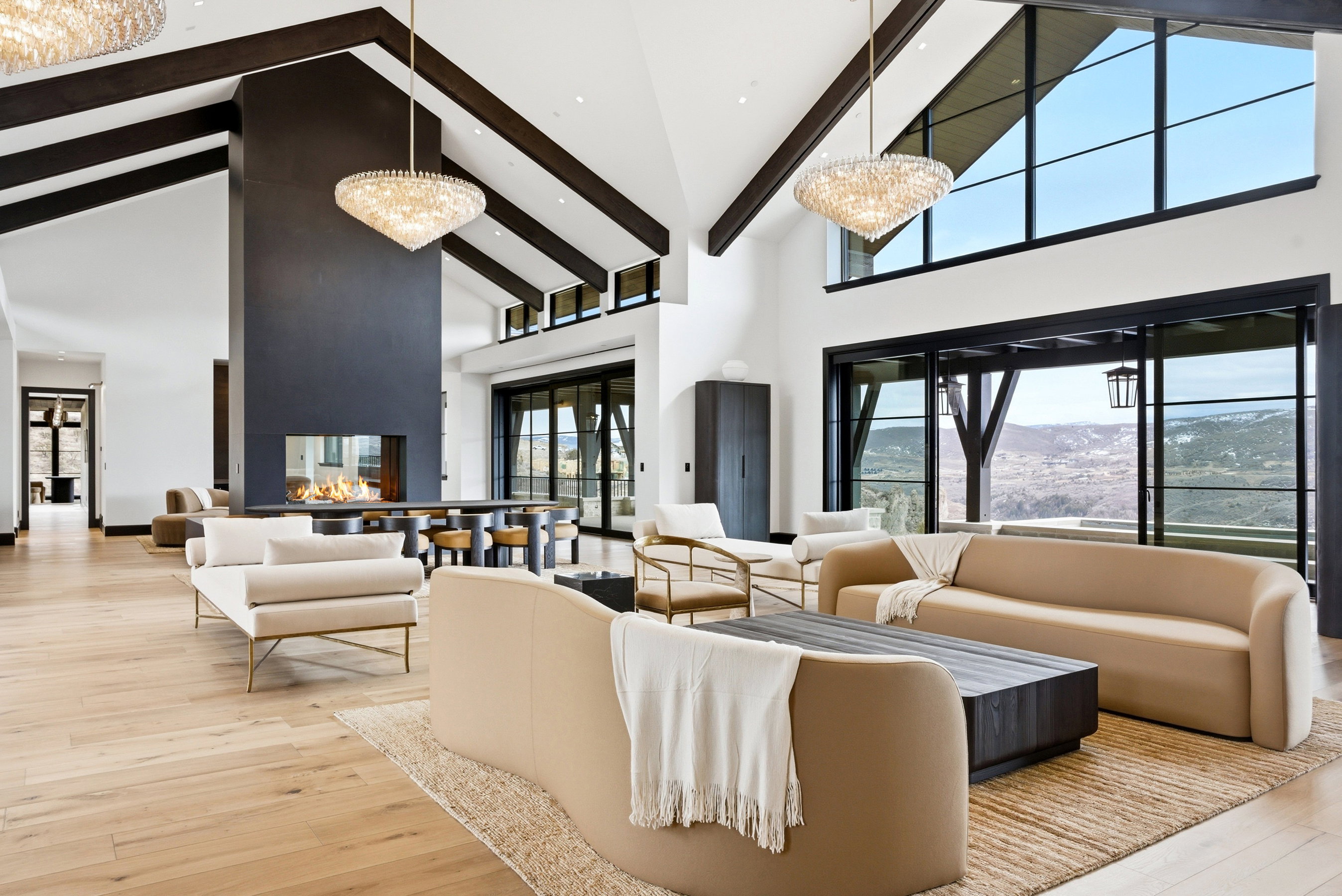 Spacious living area featuring high vaulted ceilings with exposed wood beams, wood-finish flooring, and a floor-to-ceiling fireplace with a glass-enclosed firebox