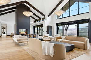 Spacious living area featuring high vaulted ceilings with exposed wood beams, wood-finish flooring, and a floor-to-ceiling fireplace with a glass-enclosed firebox