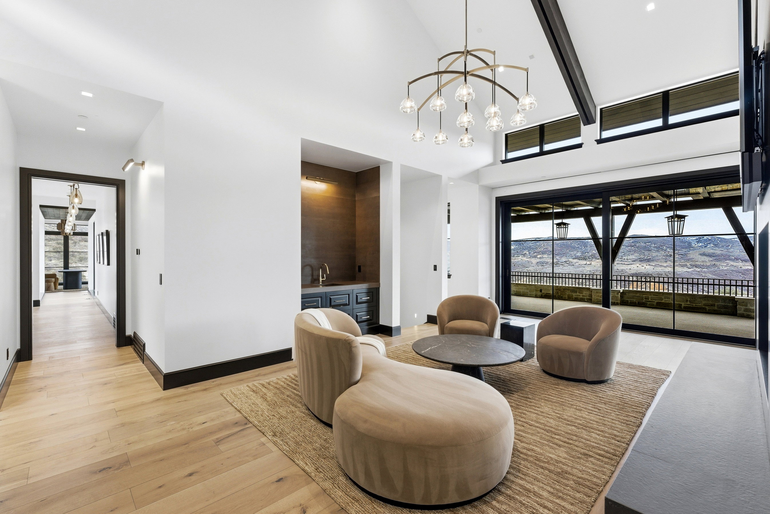 Spacious interior featuring a vaulted ceiling with exposed beams, wood-finish flooring, and a contemporary chandelier