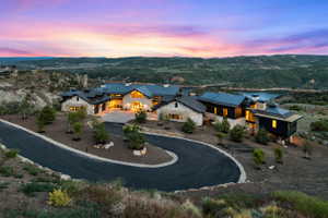 Expansive estate featuring a stone and dark wood exterior, multiple gables, a paved driveway, mature landscaping, and an elevated position overlooking a body of water