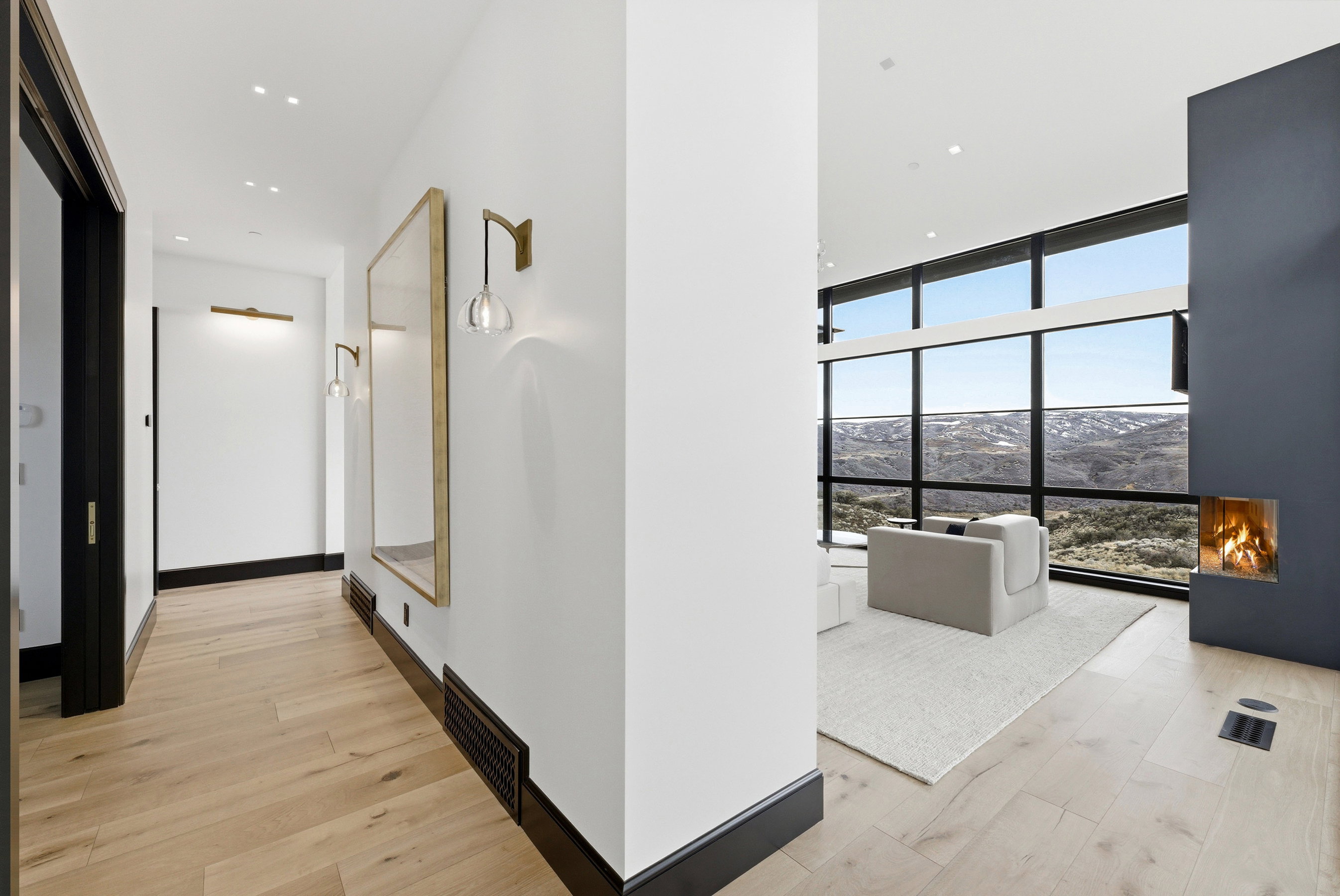Open concept living space featuring wide plank wood-finish flooring, a contemporary built-in fireplace, and full-height windows with black frames