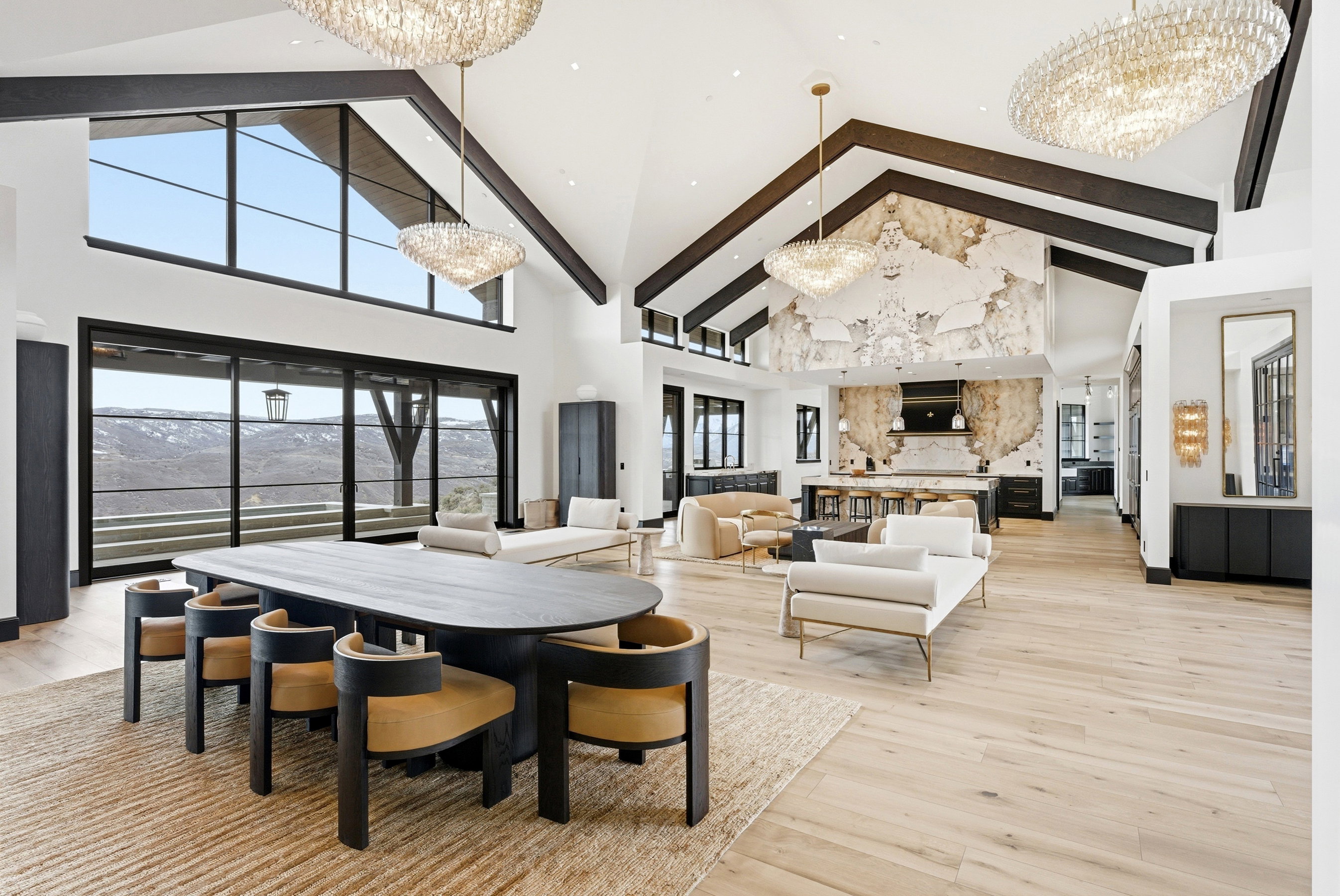 Expansive open-concept living area featuring a vaulted ceiling with exposed beams, wood-finish flooring, and large sliding glass doors