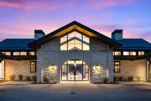 Stone facade residence featuring a prominent arched entrance with glass paneled double doors, a gabled roofline, and an expansive concrete driveway