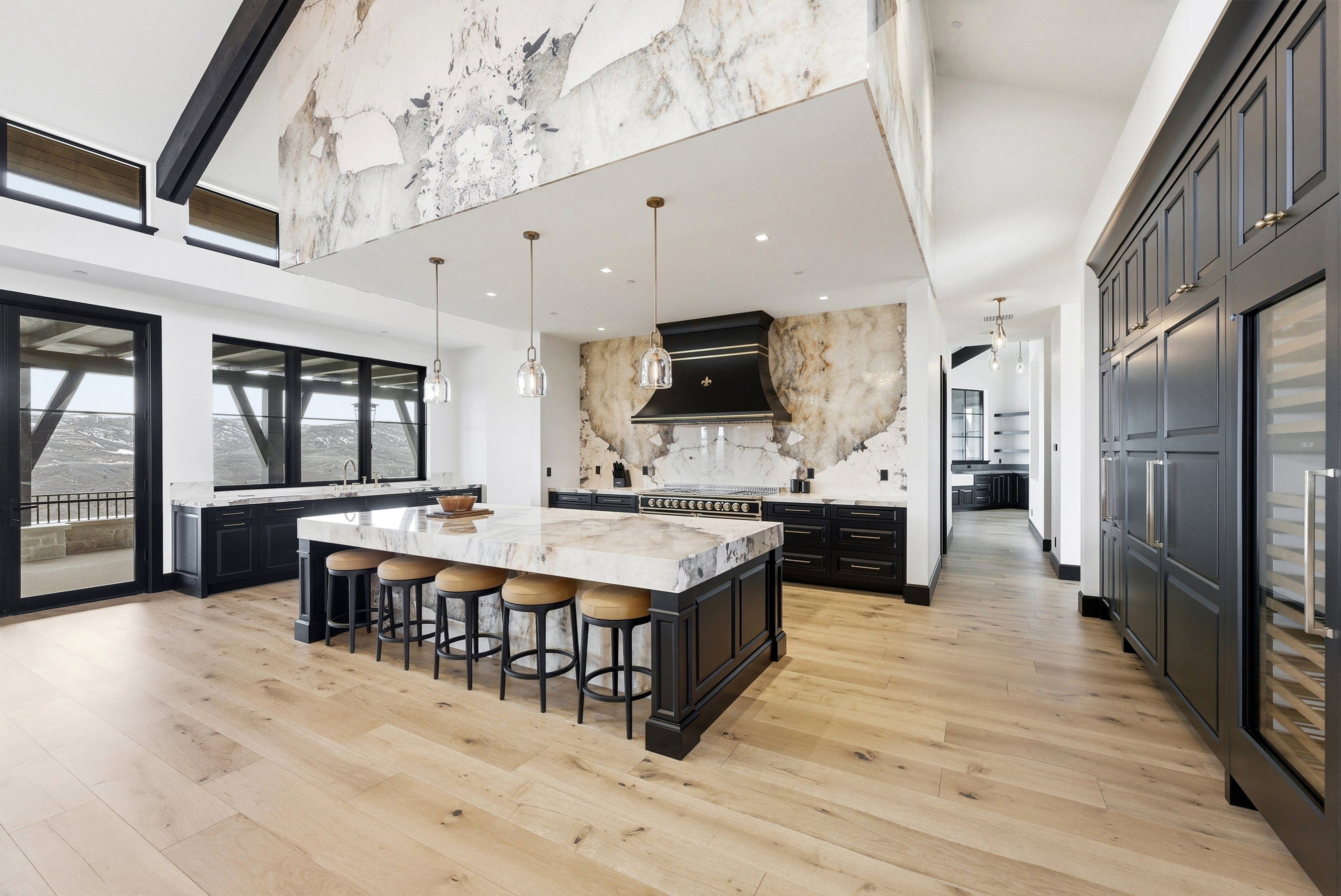 Expansive kitchen featuring a large central island with a stone countertop, custom black cabinetry, and light wood-finish flooring