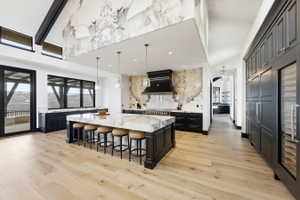 Expansive kitchen featuring a large central island with a stone countertop, custom black cabinetry, and light wood-finish flooring