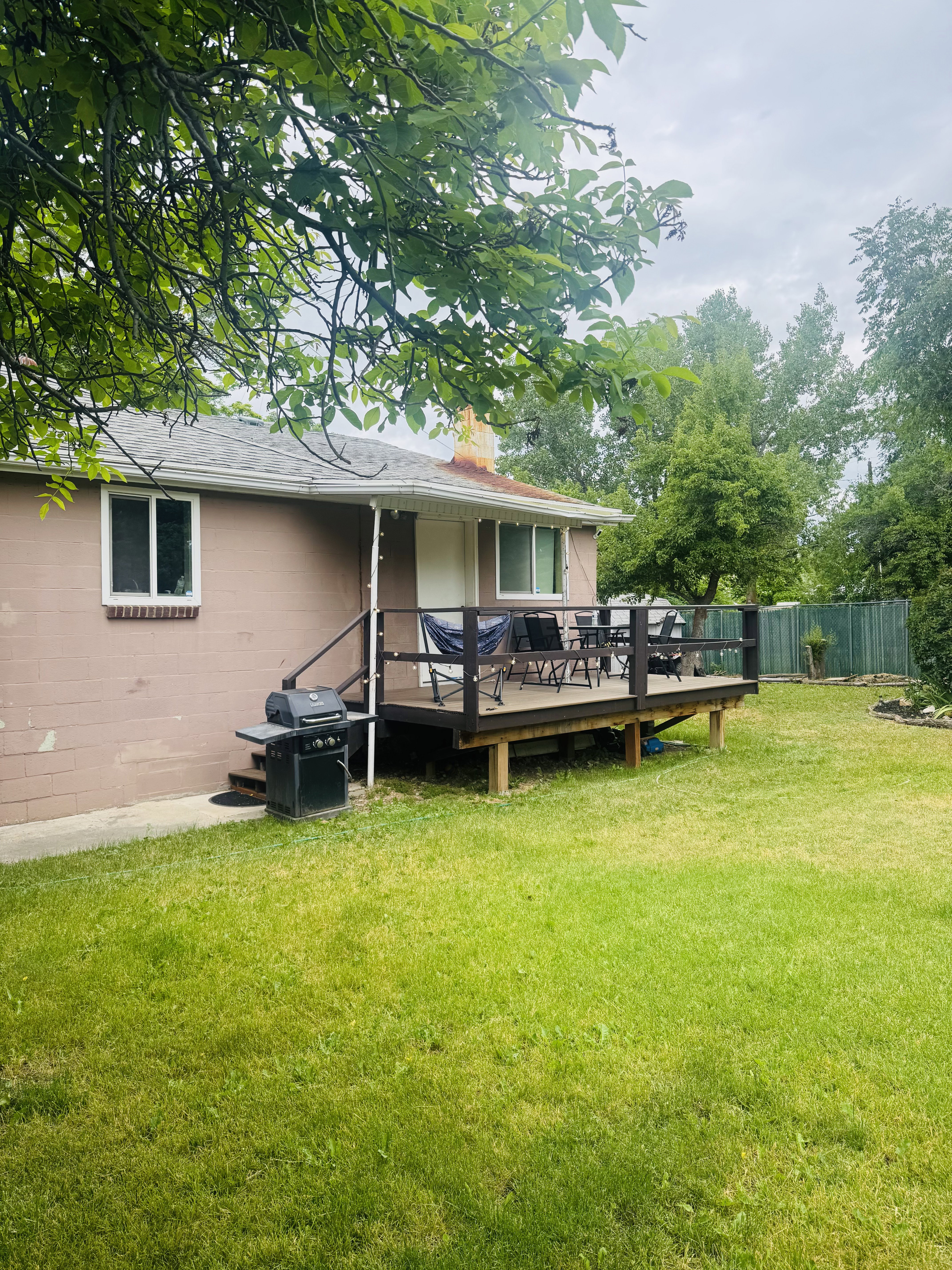 Exterior featuring a spacious wood deck, manicured lawn, and mature trees