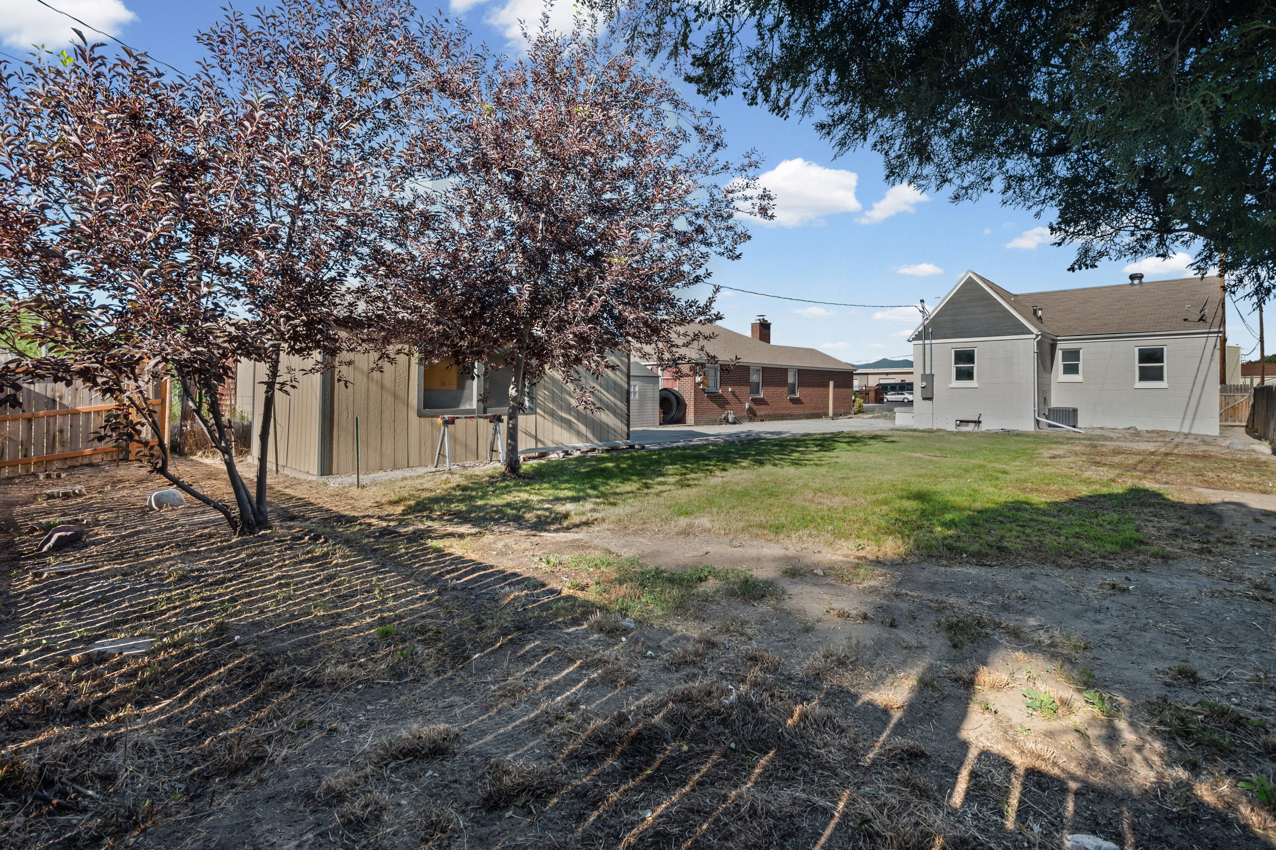 Expansive backyard featuring a partial lawn area, mature deciduous trees, and a wood privacy fence