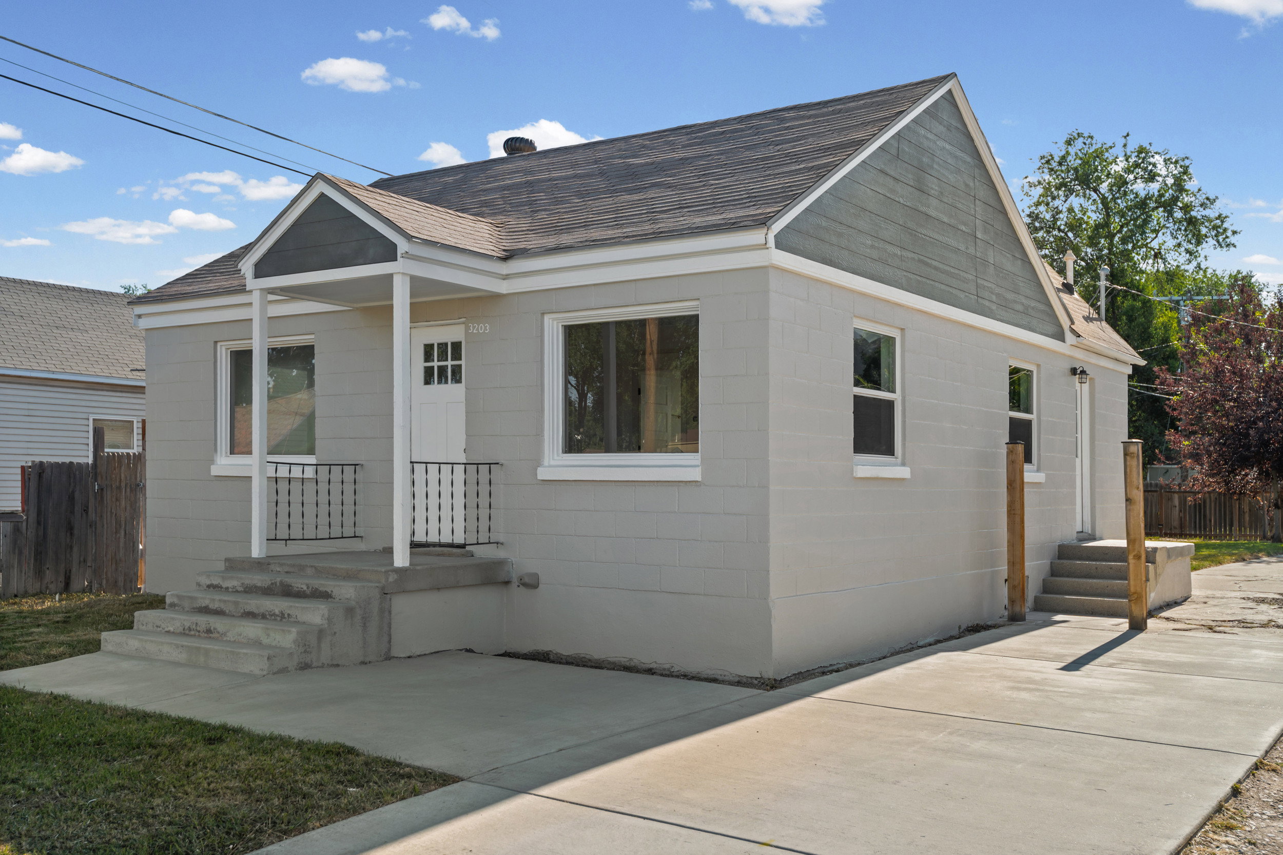 Exterior featuring light gray siding, a covered front entry with white columns, black metal railings, a white paneled front door with glass inserts, and a concrete driveway