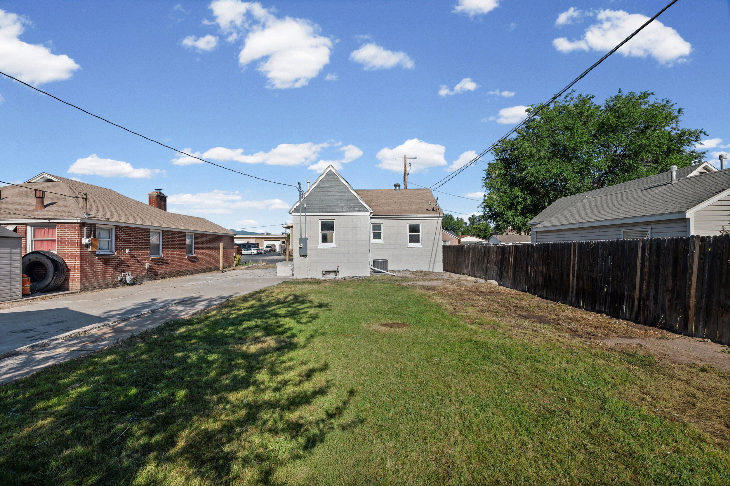 Expansive grassy yard with partial fencing and a two-story residence featuring a light gray exterior and white window trim