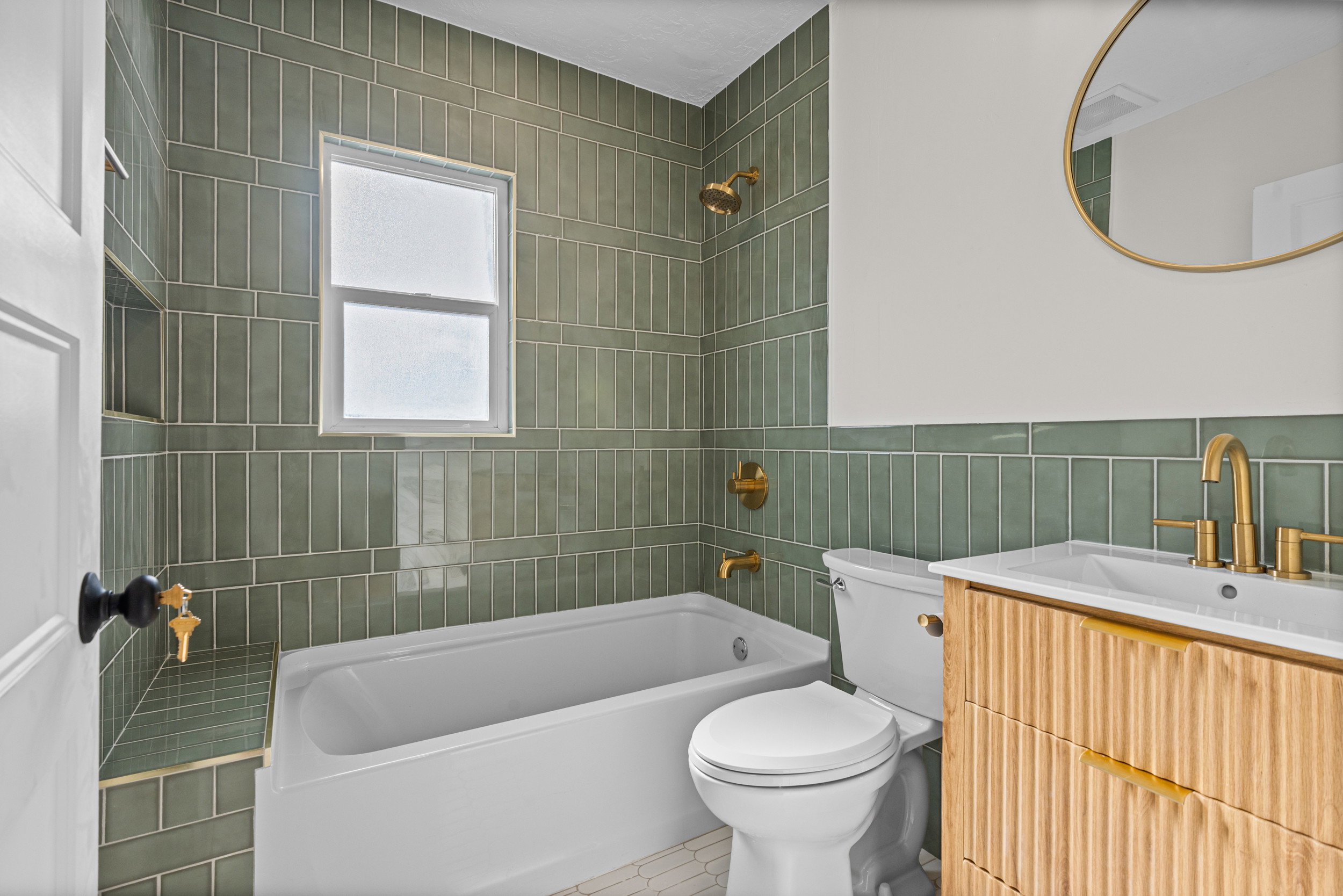 Bathroom featuring a white bathtub, green tile surround, and gold-finish fixtures