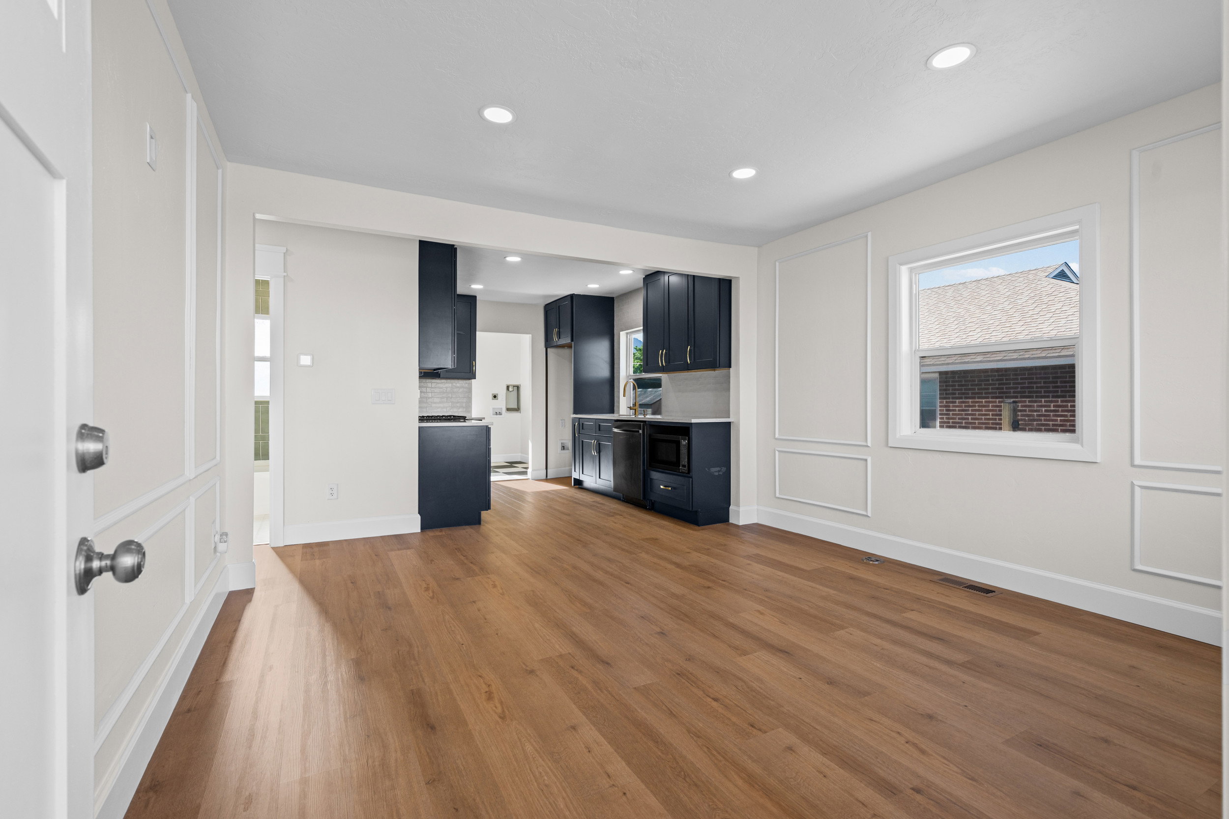 Expansive living area with wood-finish flooring, recessed lighting, decorative wall paneling, and an open archway to the kitchen