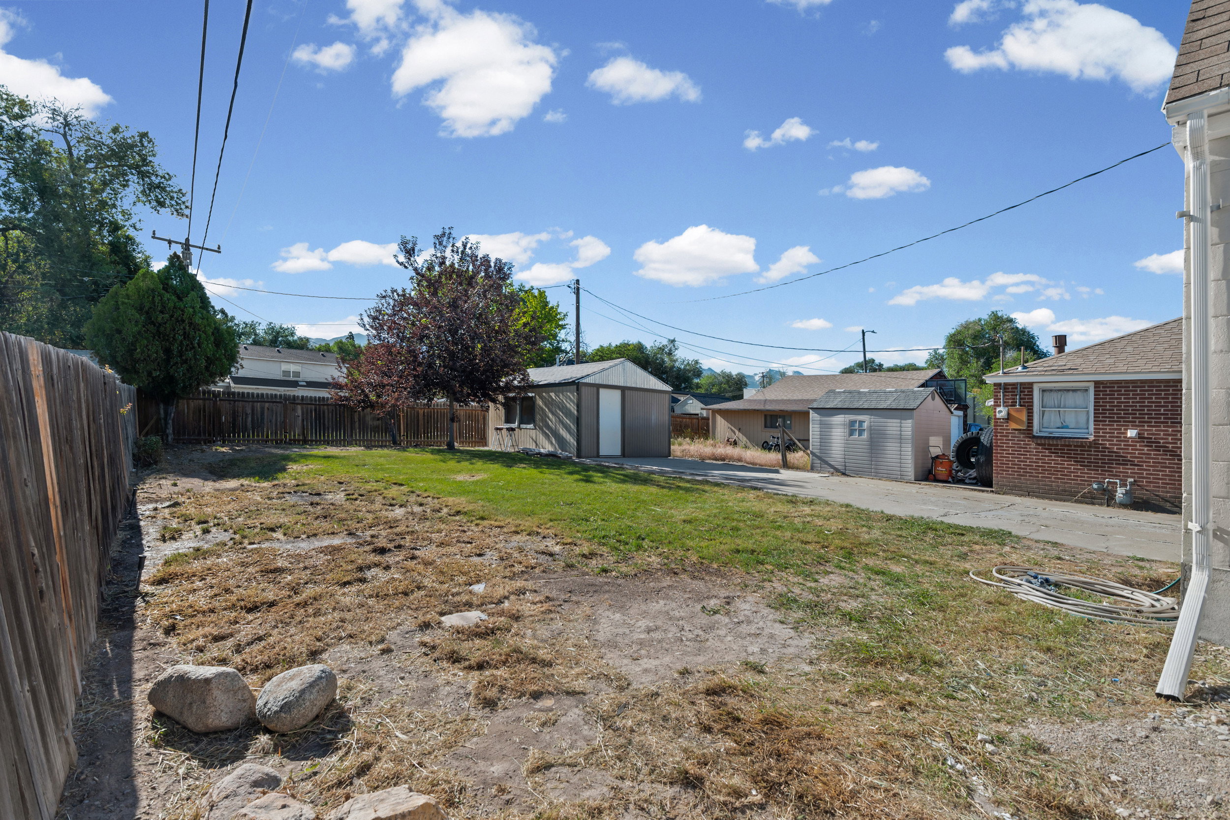 Expansive rear yard featuring a partial grass area, a wood privacy fence, and two storage sheds