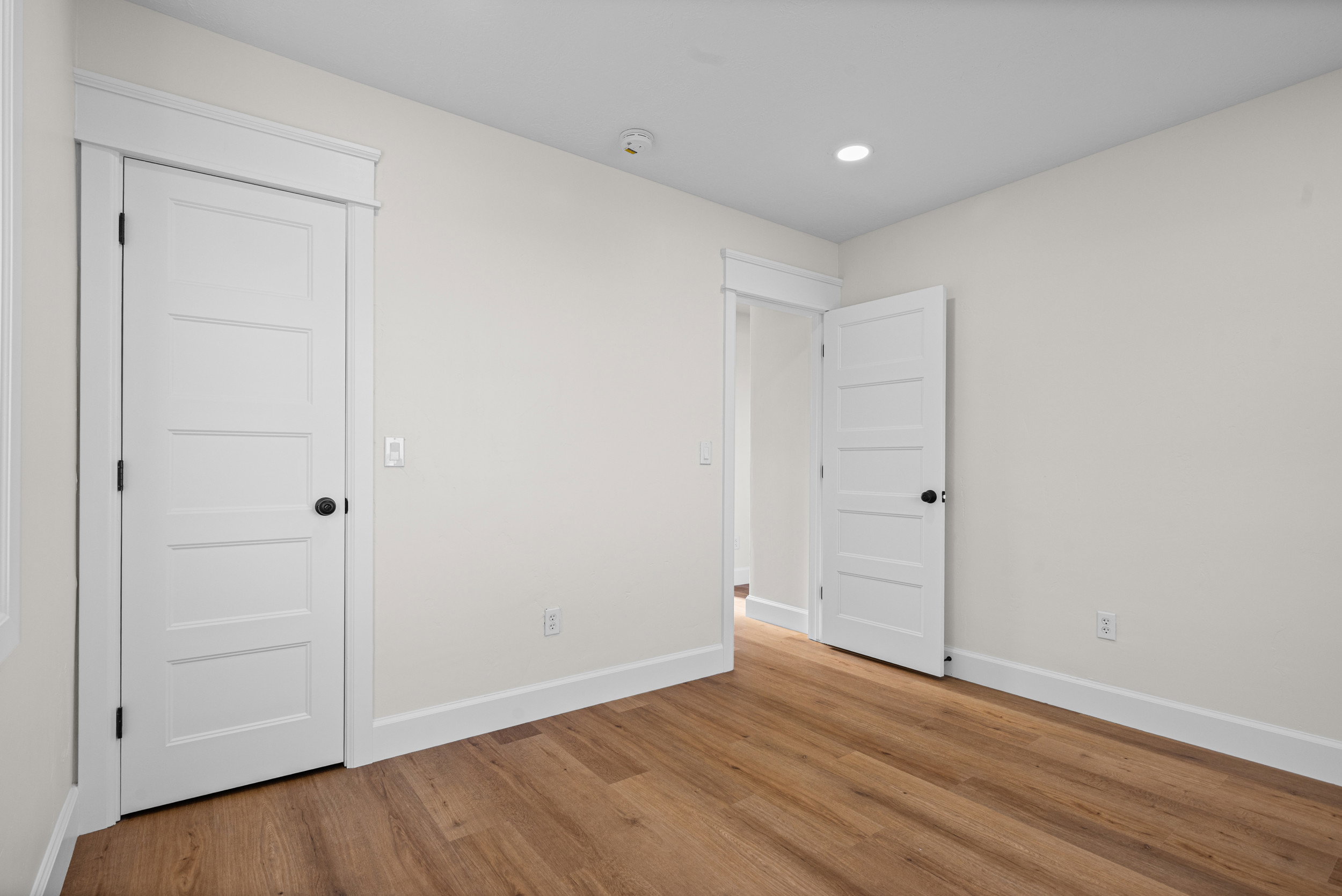 Neutral-toned room featuring wood-finish flooring, white baseboards, and white four-panel doors with black hardware