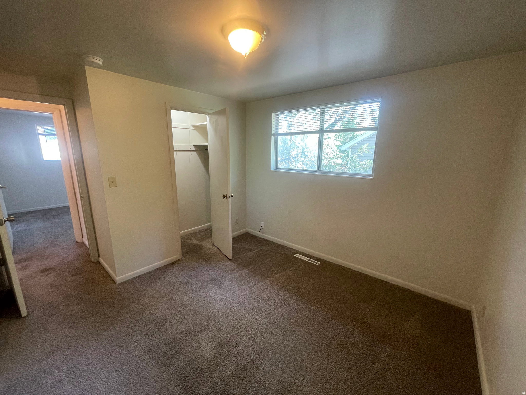 Bedroom featuring neutral carpeting, a double-hung window with blinds, and an open closet with shelving and a hanging rod