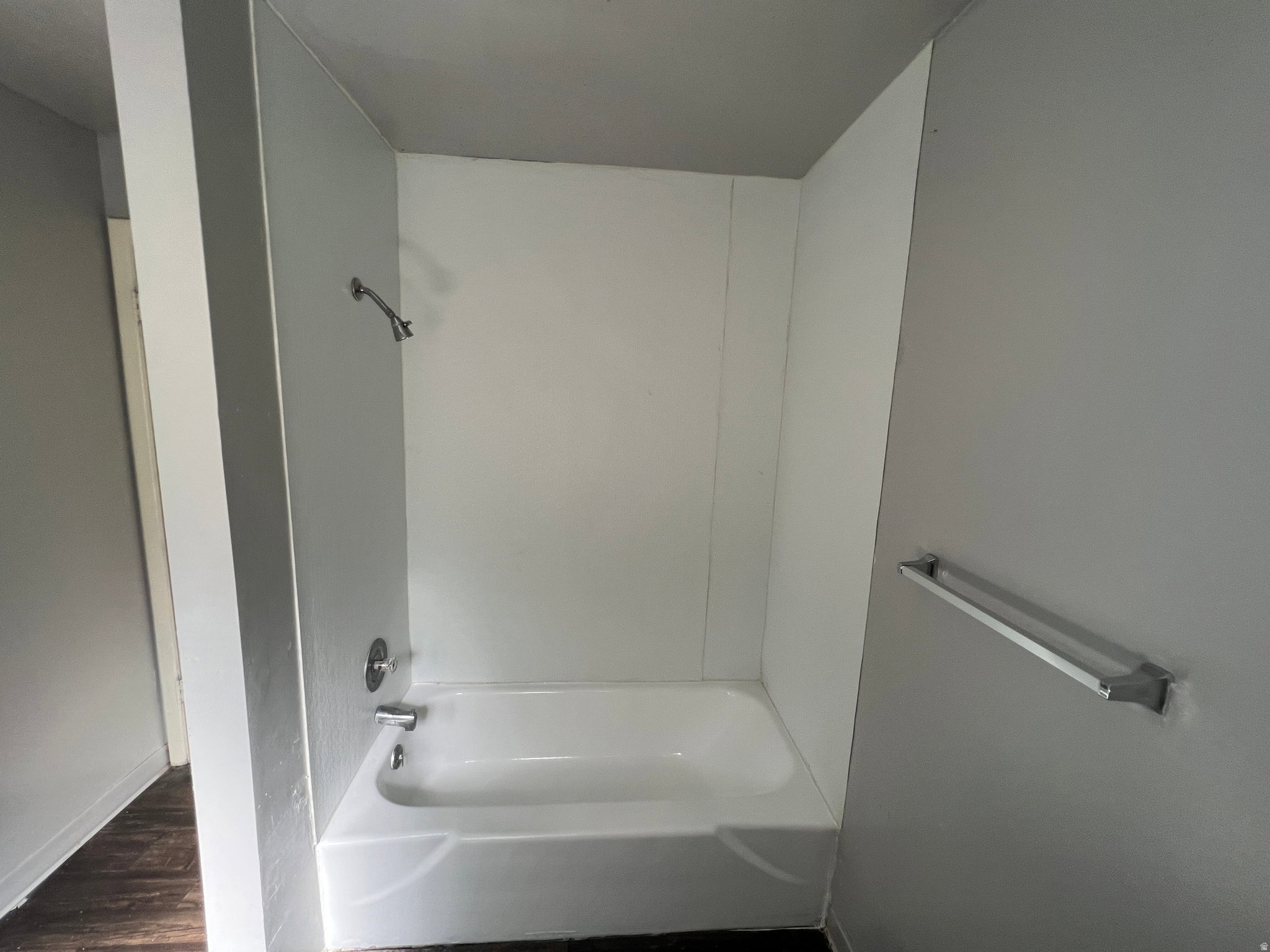 White bathtub and shower surround with chrome fixtures, set against light gray walls