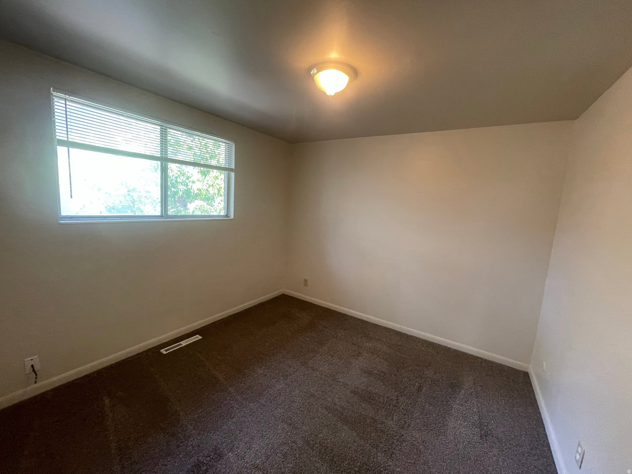 Spacious room featuring neutral wall tones and dark carpeting