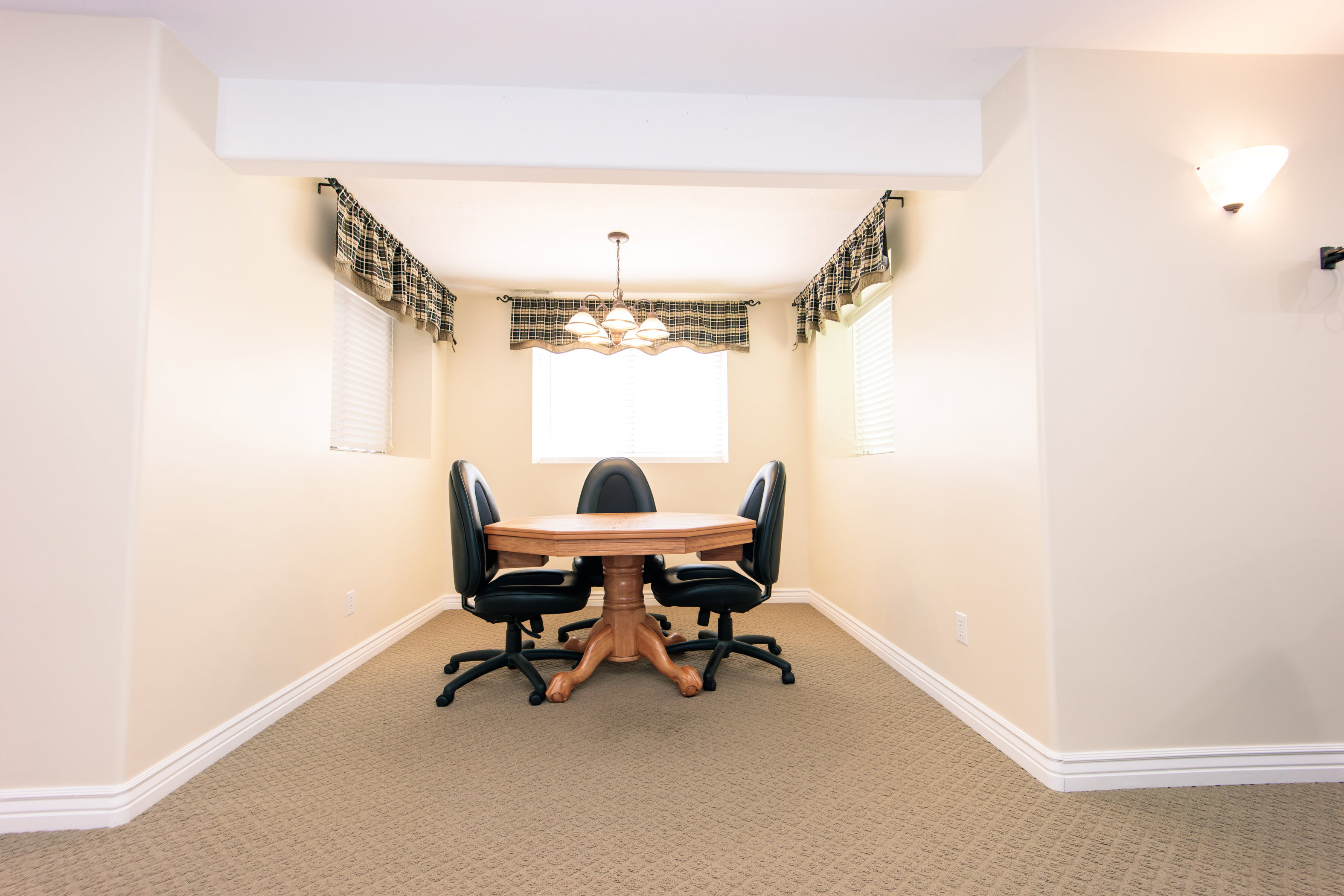 Carpeted area featuring two windows with blinds and valances, illuminated by a central chandelier and a wall sconce