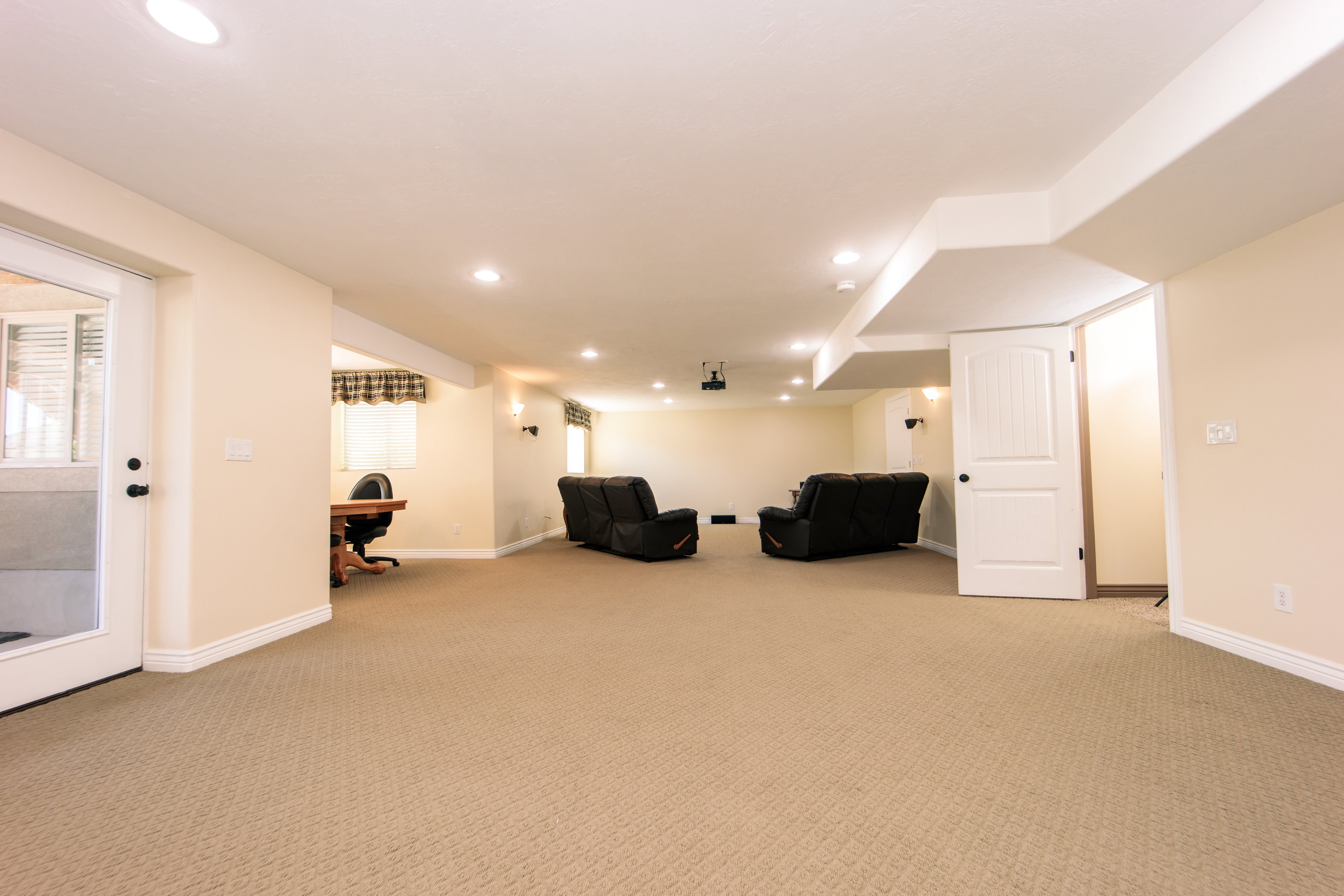 Spacious carpeted room featuring recessed lighting, a built-in projector, a light-colored accent wall, white trim, and a white interior door