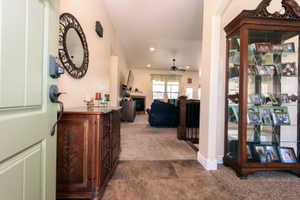 Entryway with tile flooring opening to a carpeted living space featuring a fireplace, a ceiling fan, and a light-colored main door