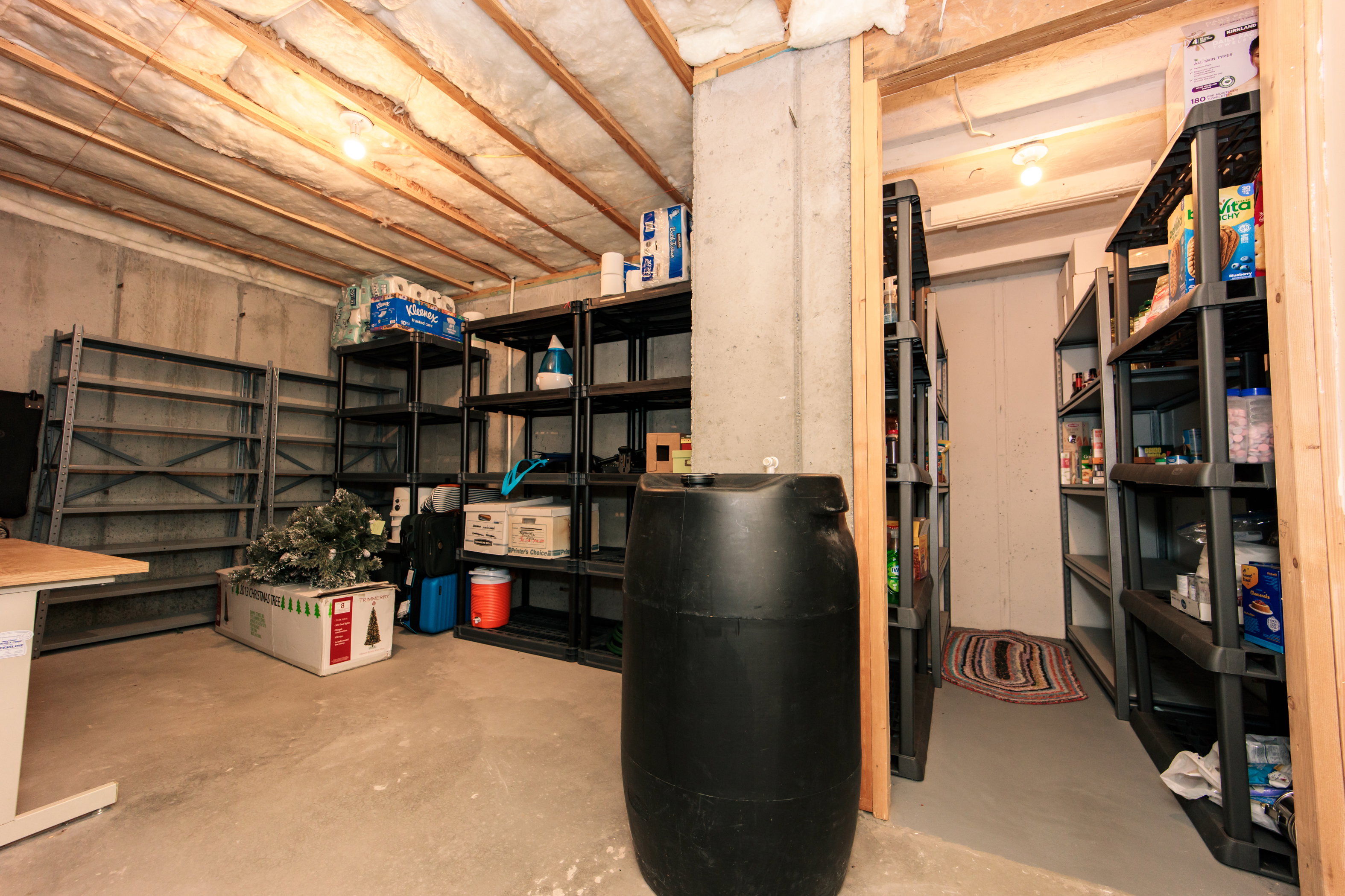 Unfinished basement space featuring exposed wood joists, concrete walls, concrete flooring, and an open doorway