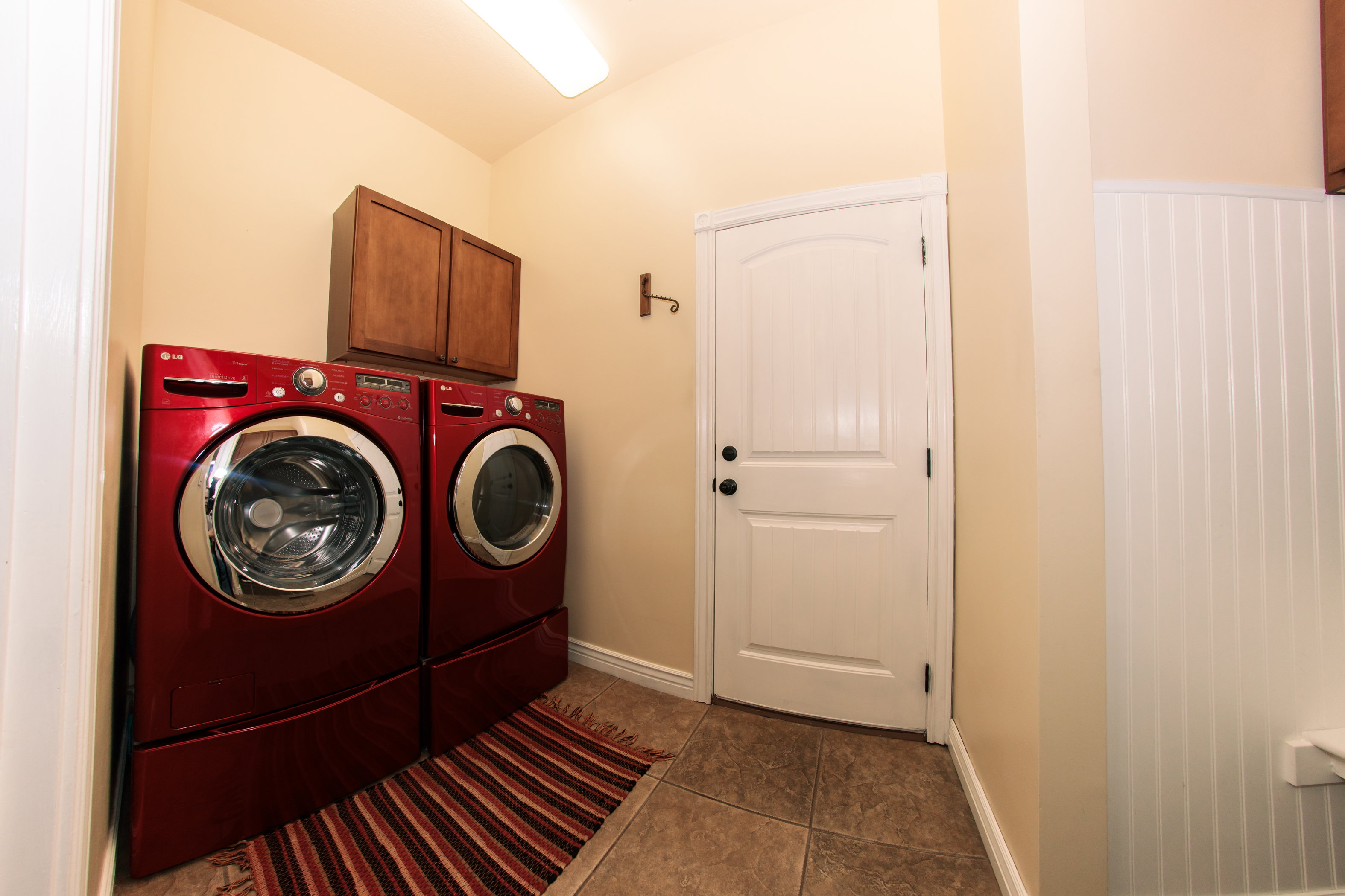 Laundry area featuring tile flooring, a wood-finish wall cabinet, and beadboard wainscoting