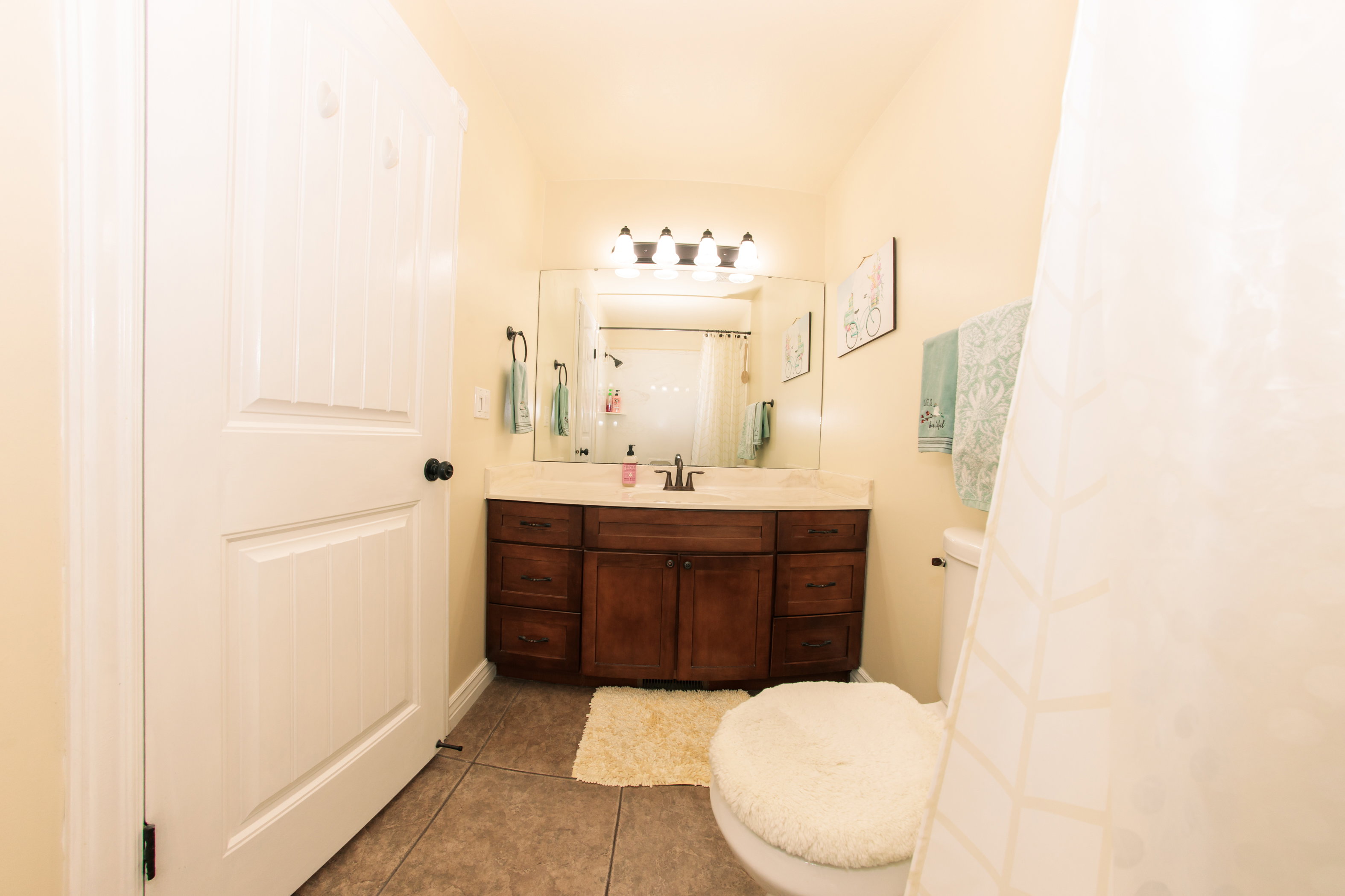 Bathroom featuring a wood-finish vanity with a light-toned countertop, a rectangular mirror, and a four-light fixture