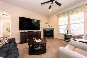 Living room featuring a corner fireplace with a dark stone surround and hearth, carpeted flooring, and a ceiling fan with integrated lighting