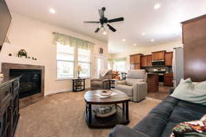 Open-concept living space featuring a gas fireplace with a stone-tile surround, neutral carpeting, and a ceiling fan with integrated lighting