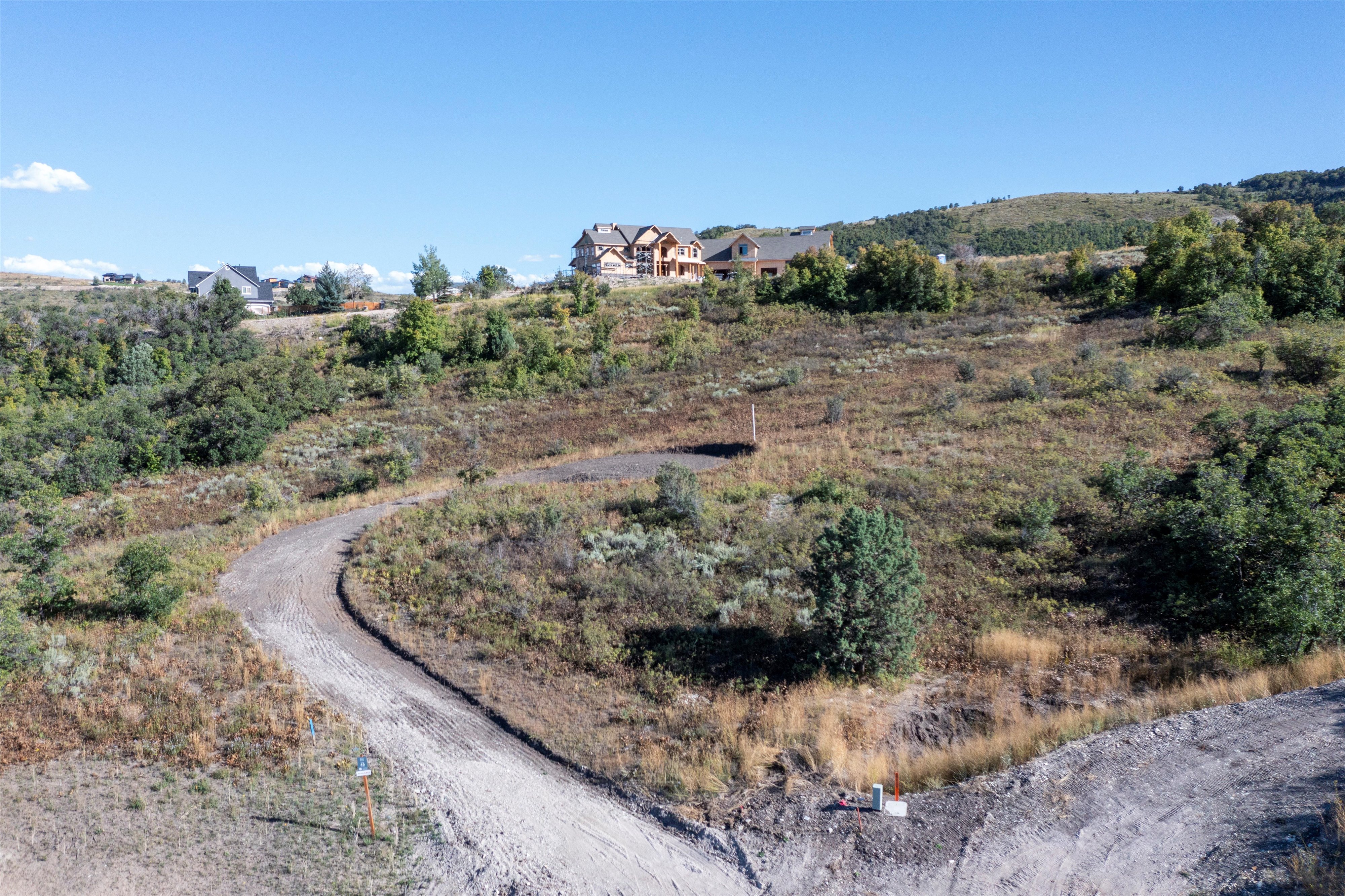 Unimproved sloped land parcel with natural vegetation and distant residential structures