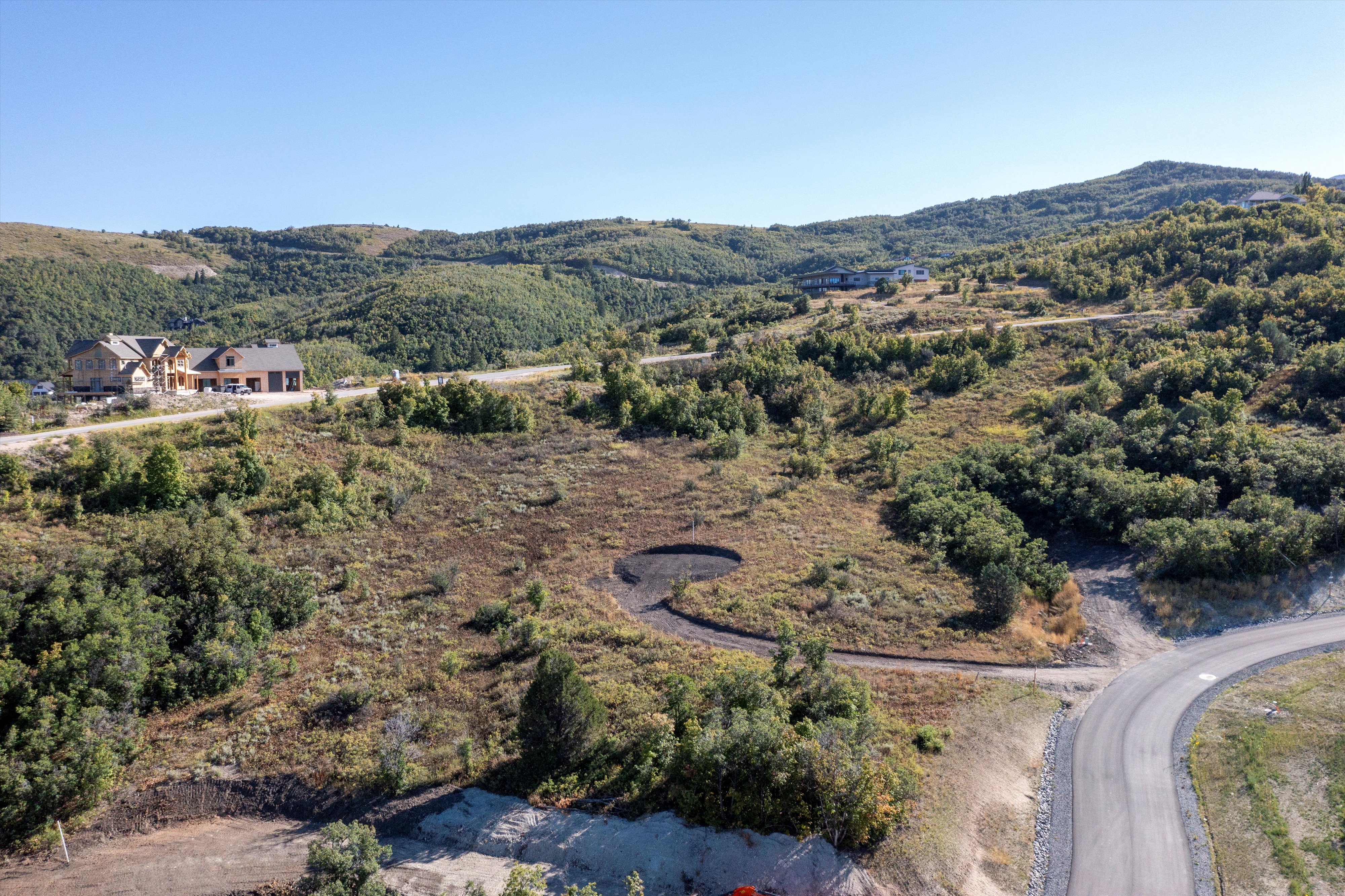 Cleared land parcel with a paved road frontage, surrounded by rolling hills and scattered mature trees