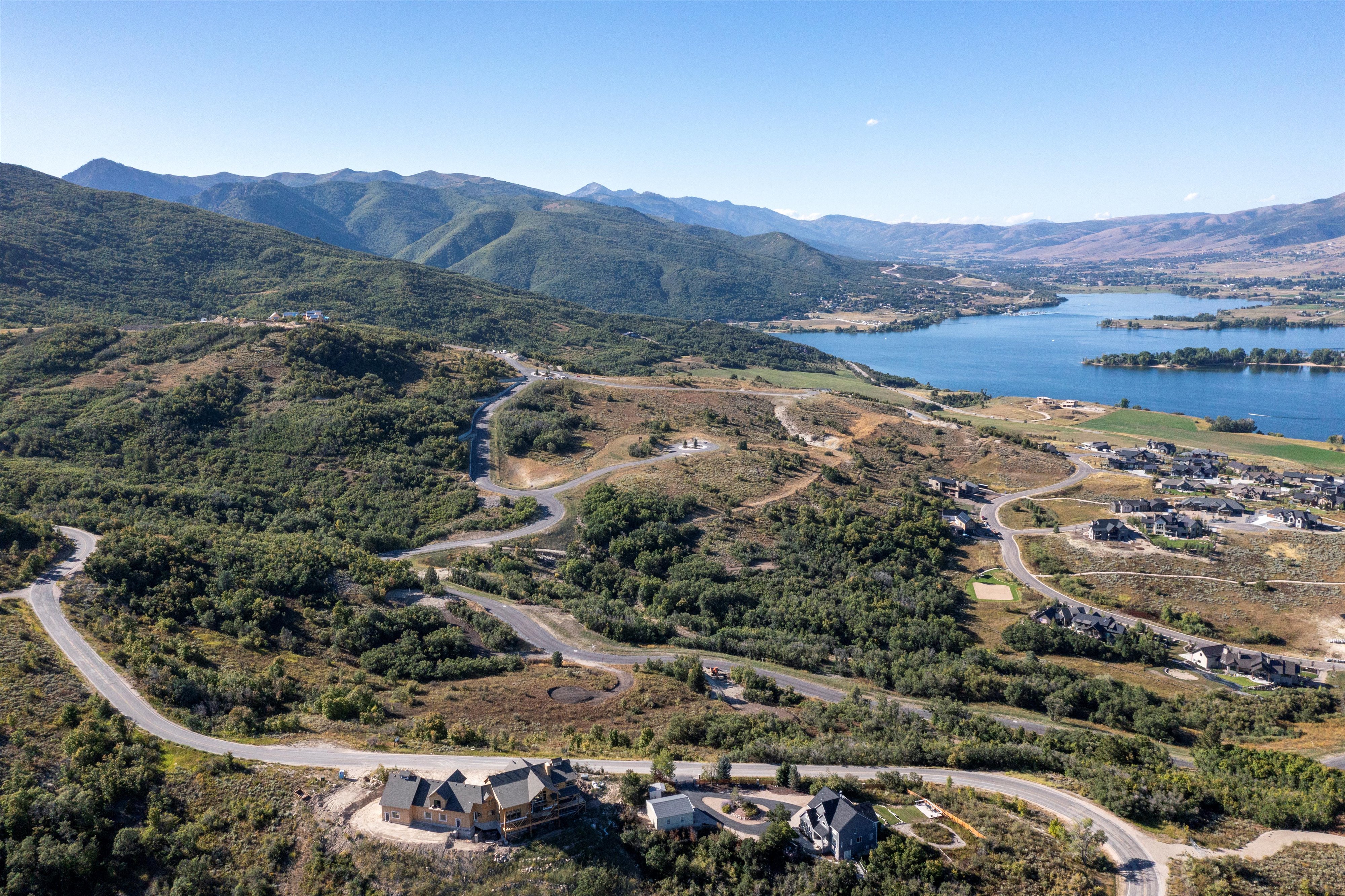 Expansive mountain landscape featuring a large body of water, several residential properties, and winding roads