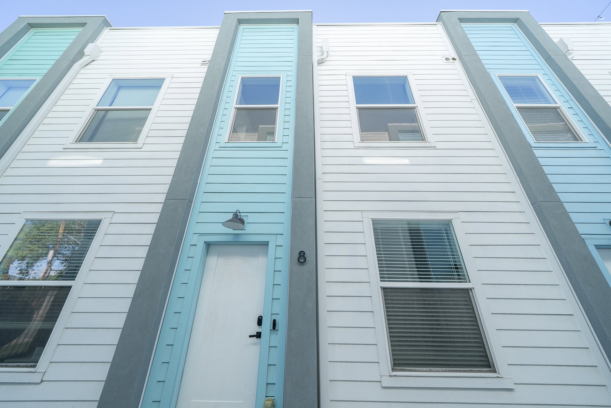 Modern townhome facade featuring white horizontal siding and prominent vertical light blue accent panels