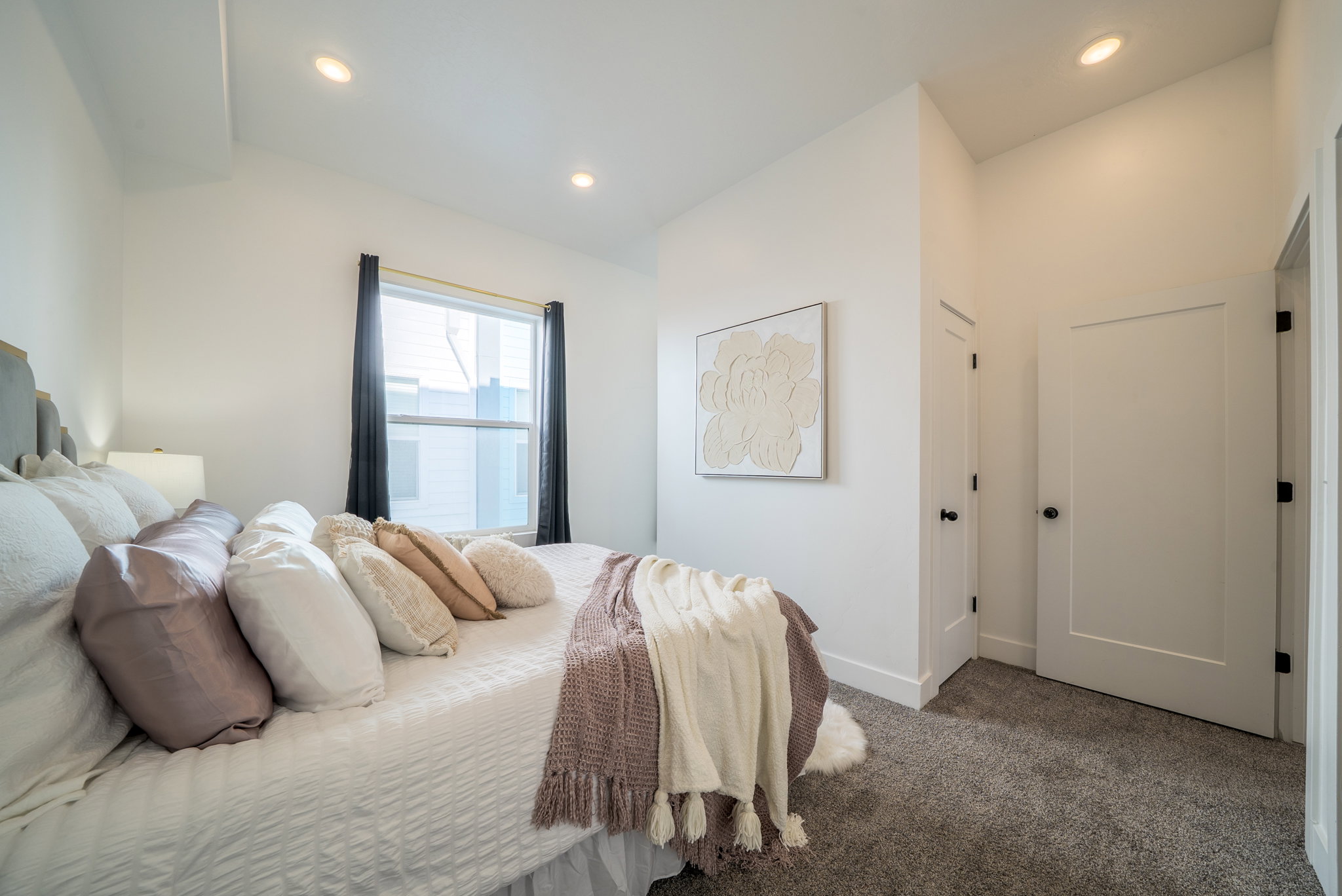 Recessed lighting illuminating a window-equipped room with tall ceilings, white walls, and gray carpet