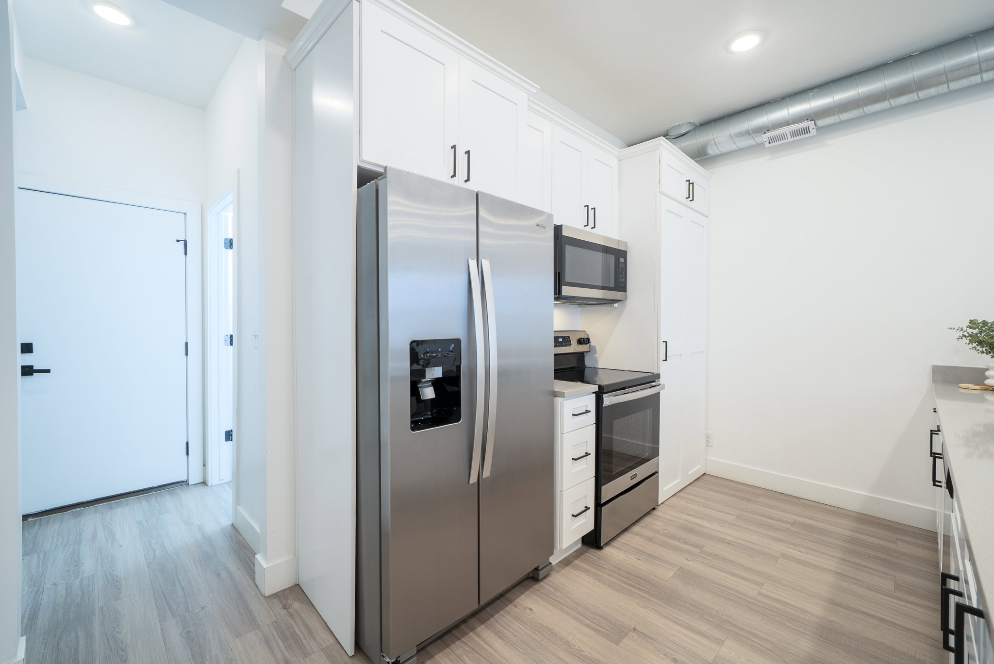 Kitchen featuring stainless steel appliances, white shaker-style cabinetry, light wood-finish flooring, and a visible industrial-style duct