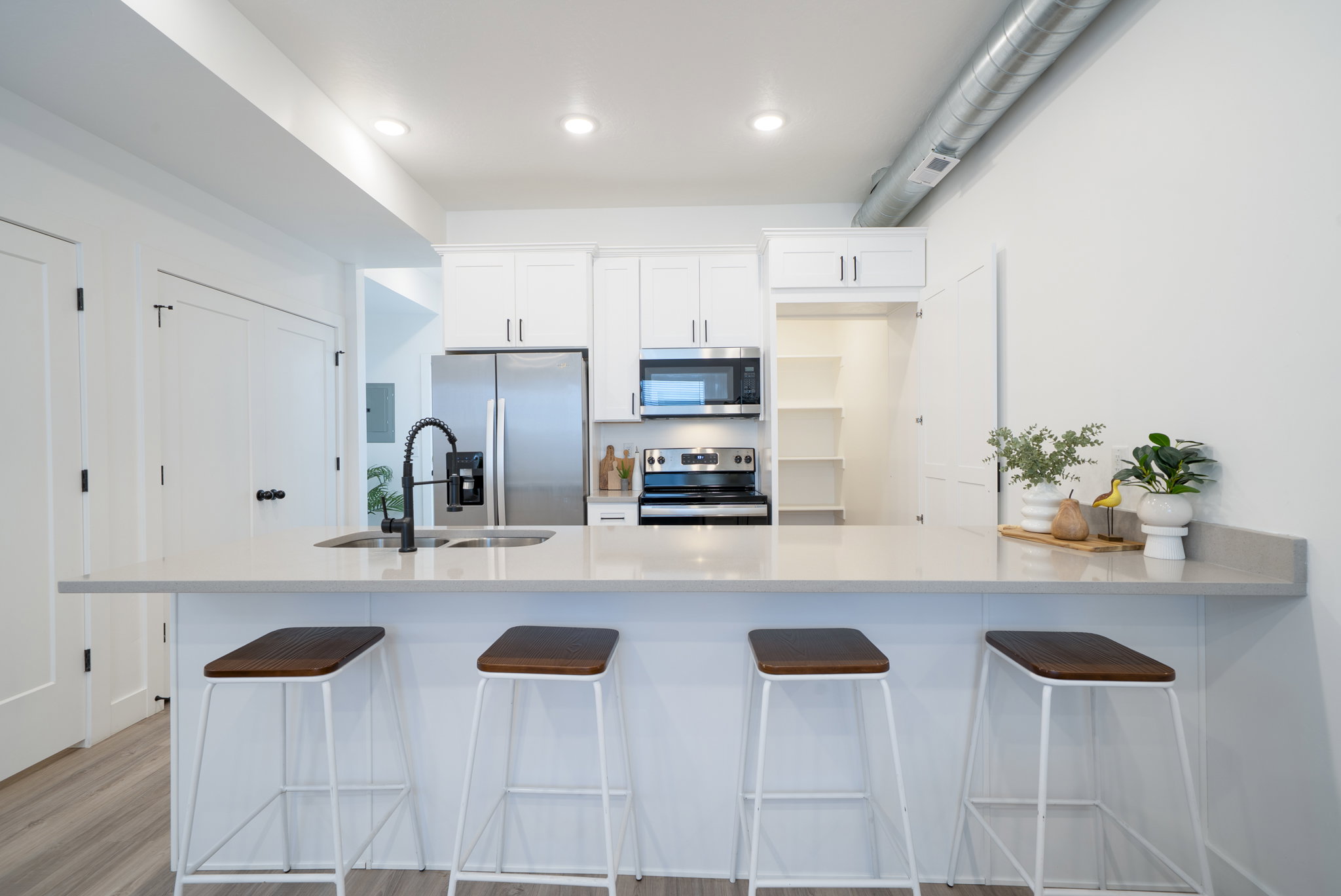 Kitchen featuring a large light-toned countertop island with seating, white cabinetry, stainless steel appliances, and wood-finish flooring