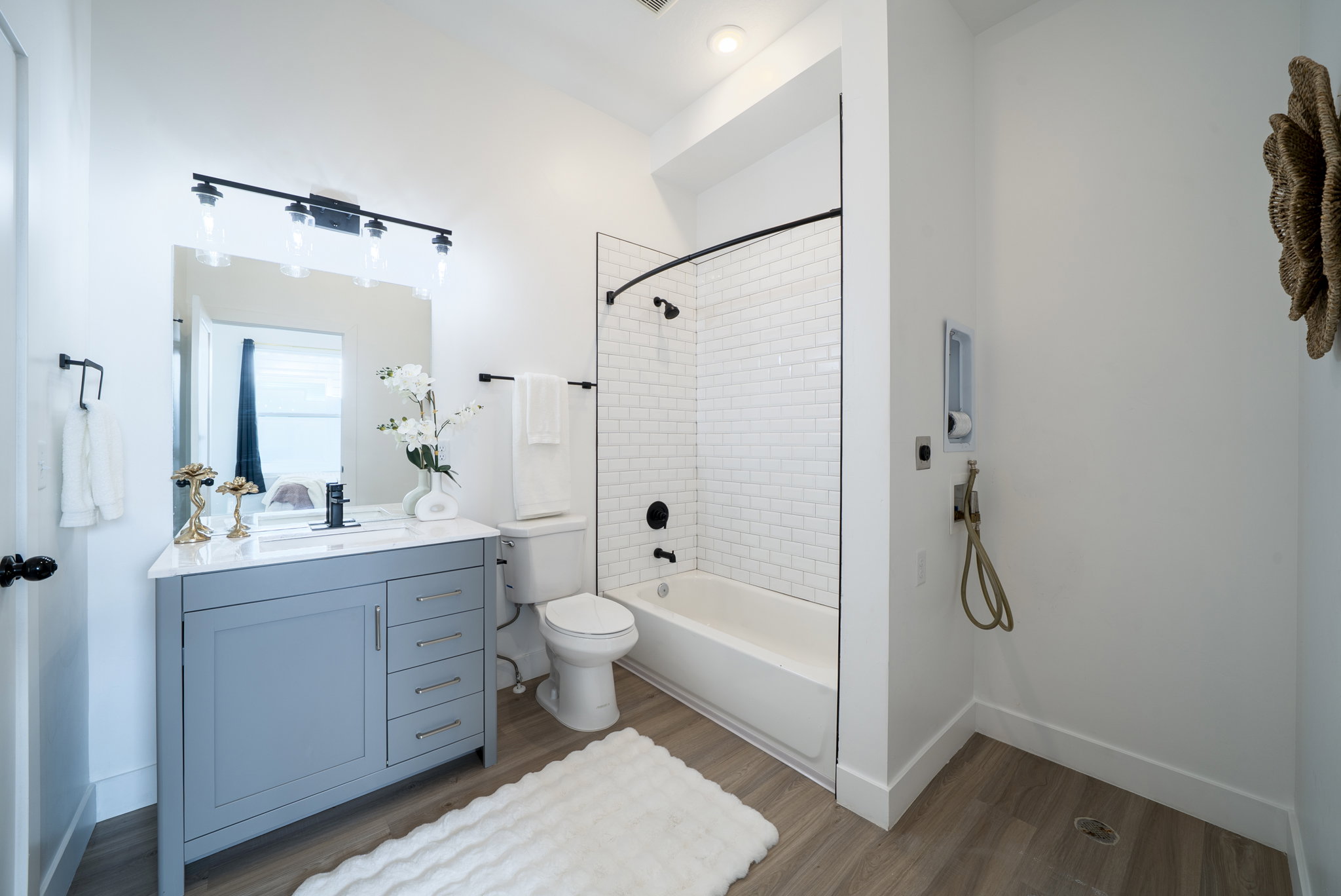 Bathroom featuring a light blue vanity with a white countertop and rectangular sink, wood-finish flooring, a white subway tile shower surround with a black-framed glass enclosure, and modern black fixtures