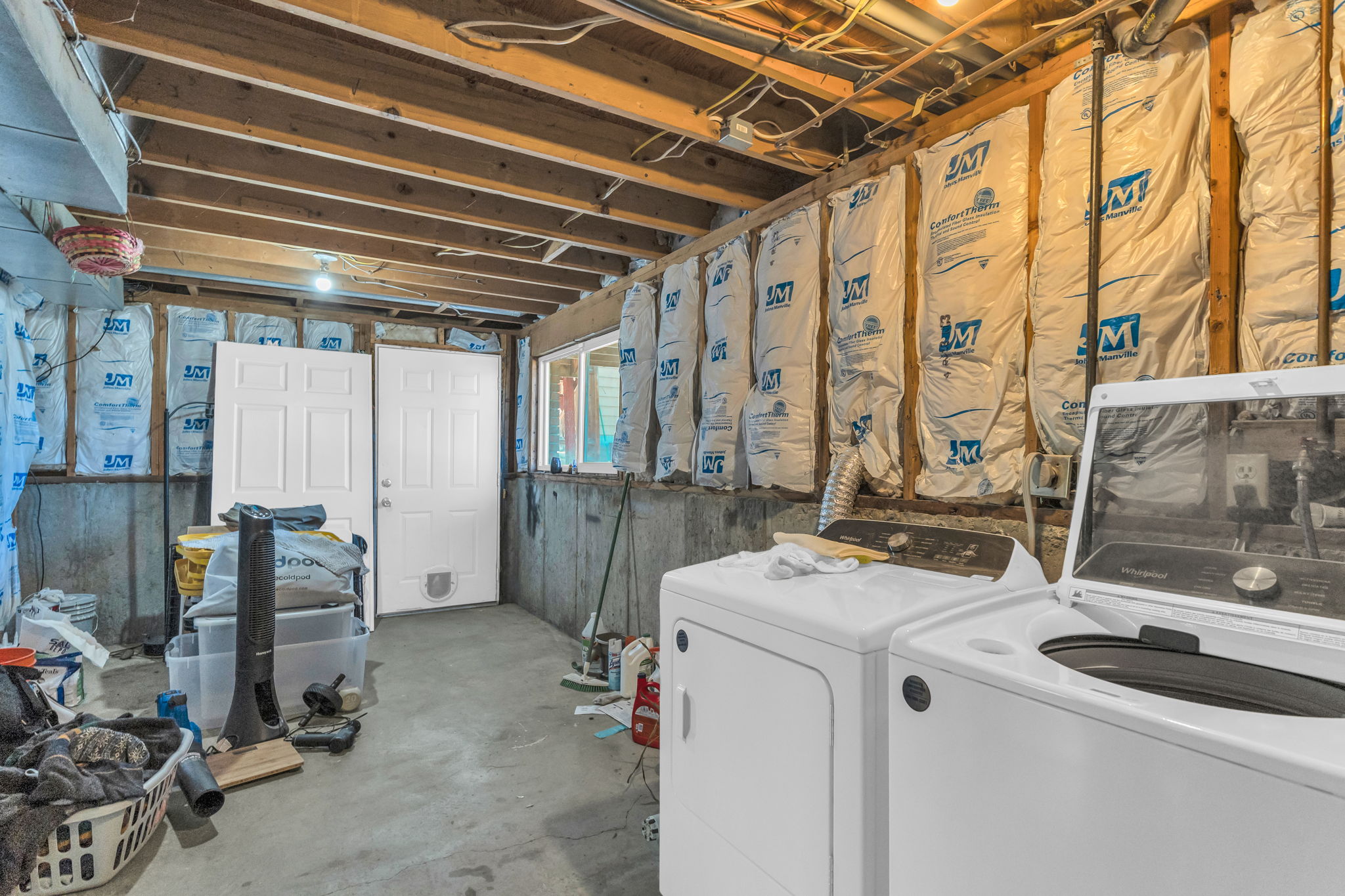 Unfinished basement space featuring exposed wood joists, partial insulation, a concrete floor, and two panel doors